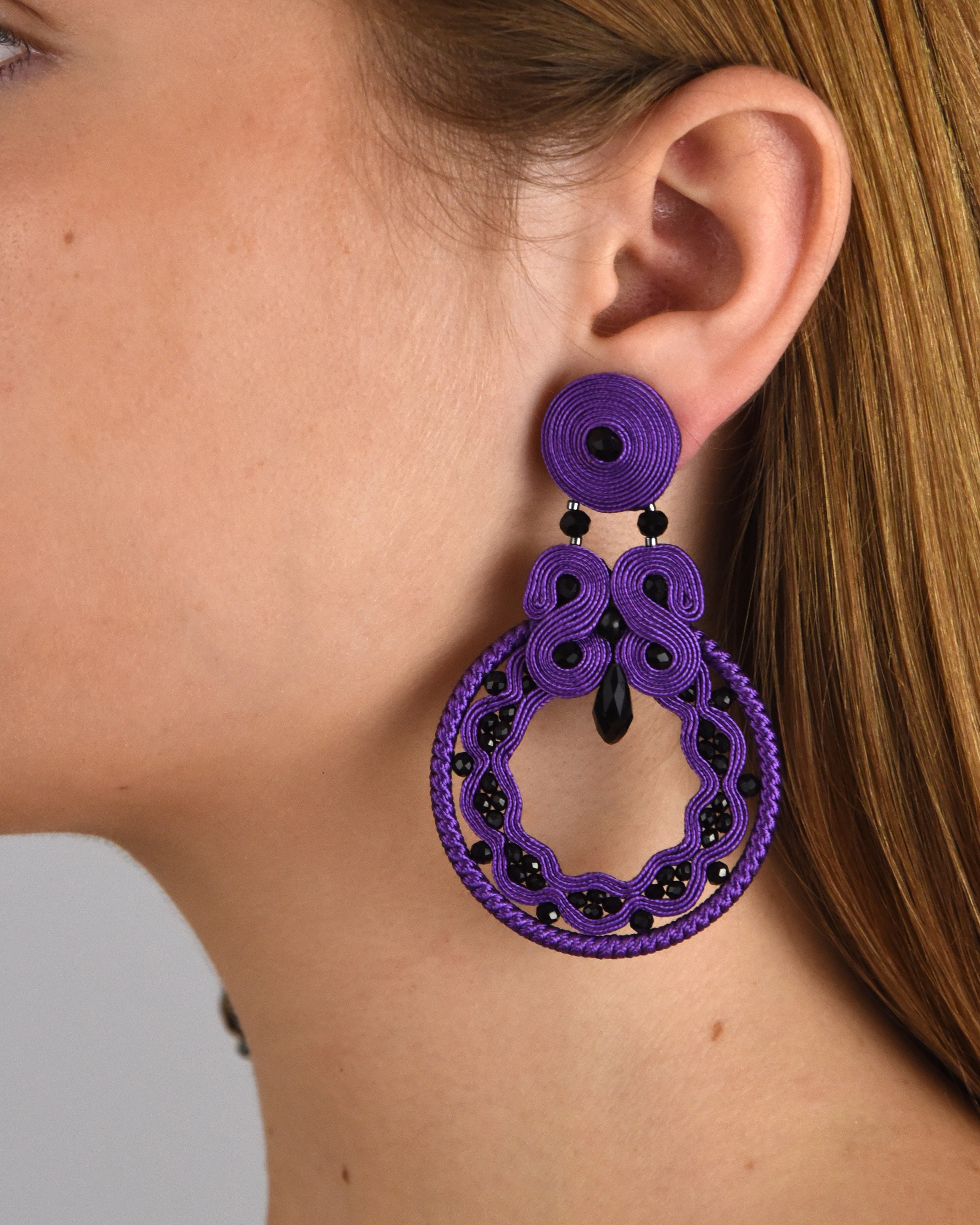 Mujer luciendo los pendientes statement Nazareno Azabache, destacando su tamaño y la intensidad del color violeta.