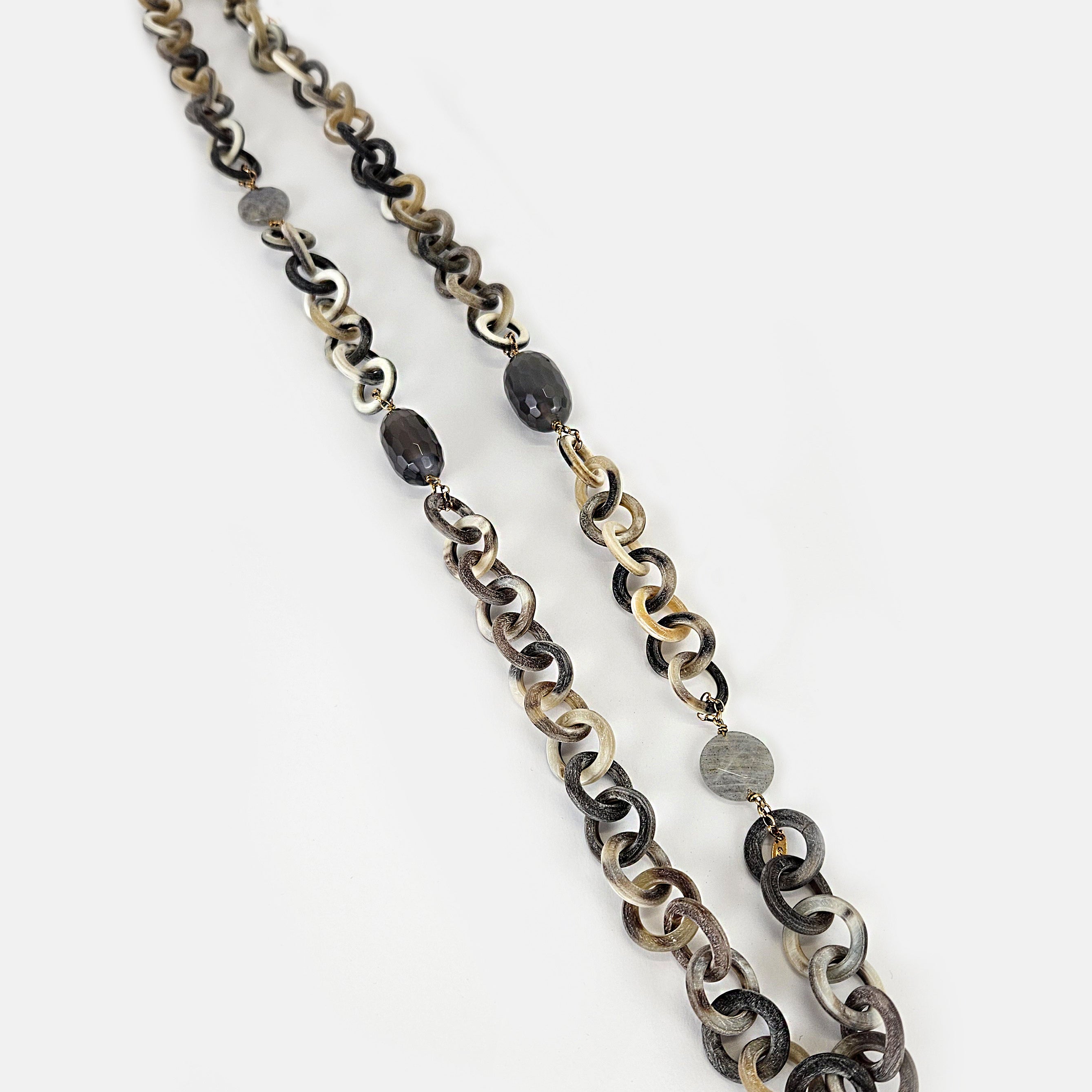 Collar largo Amlé con eslabones circulares de cuerno natural en tonos grises y crema, y piedras semipreciosas oscuras.