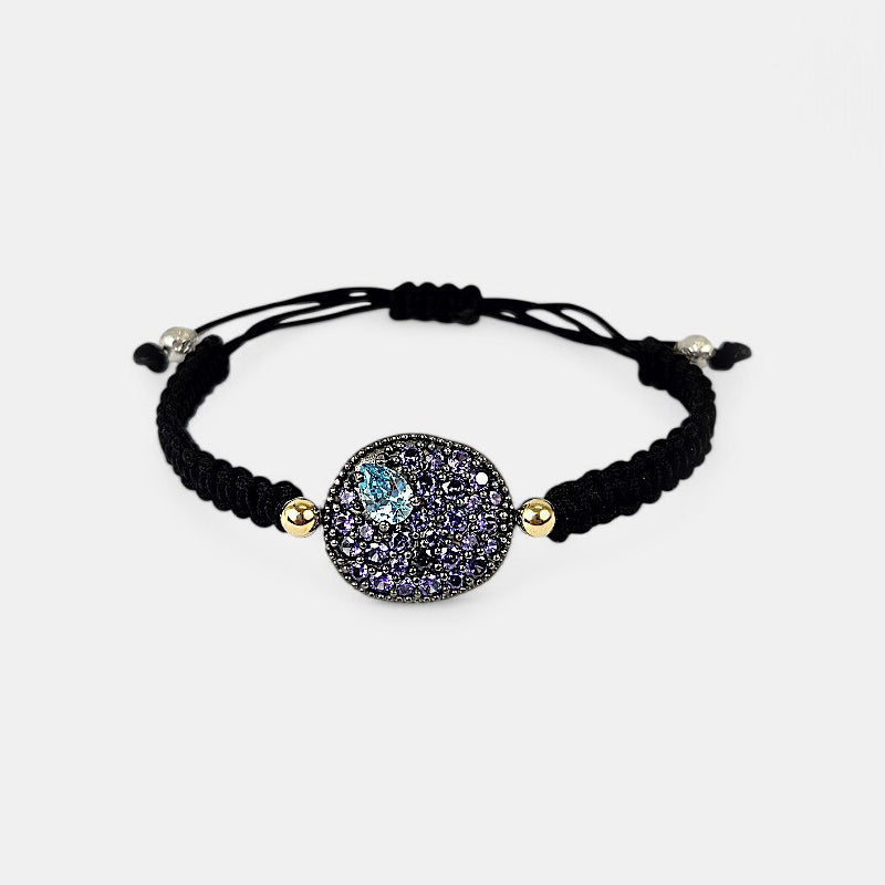 Pulsera de macramé negro Bohemme Musa con medallón de plata oxidada y pavé de circonitas violetas con detalle azul.