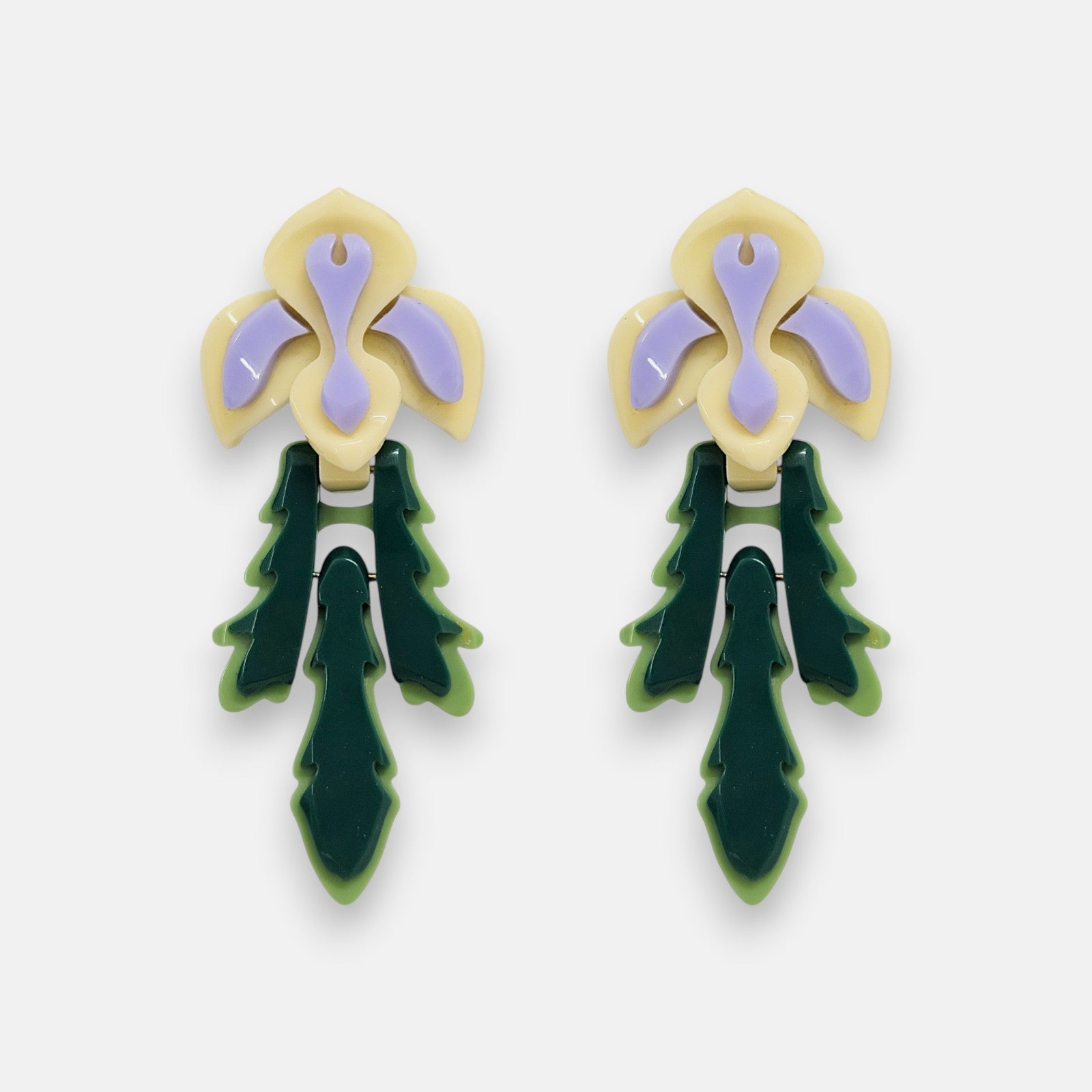 Par de pendientes "Iris" de Gissa Bicalho con diseño floral en resina crema, lila y verde sobre fondo claro.