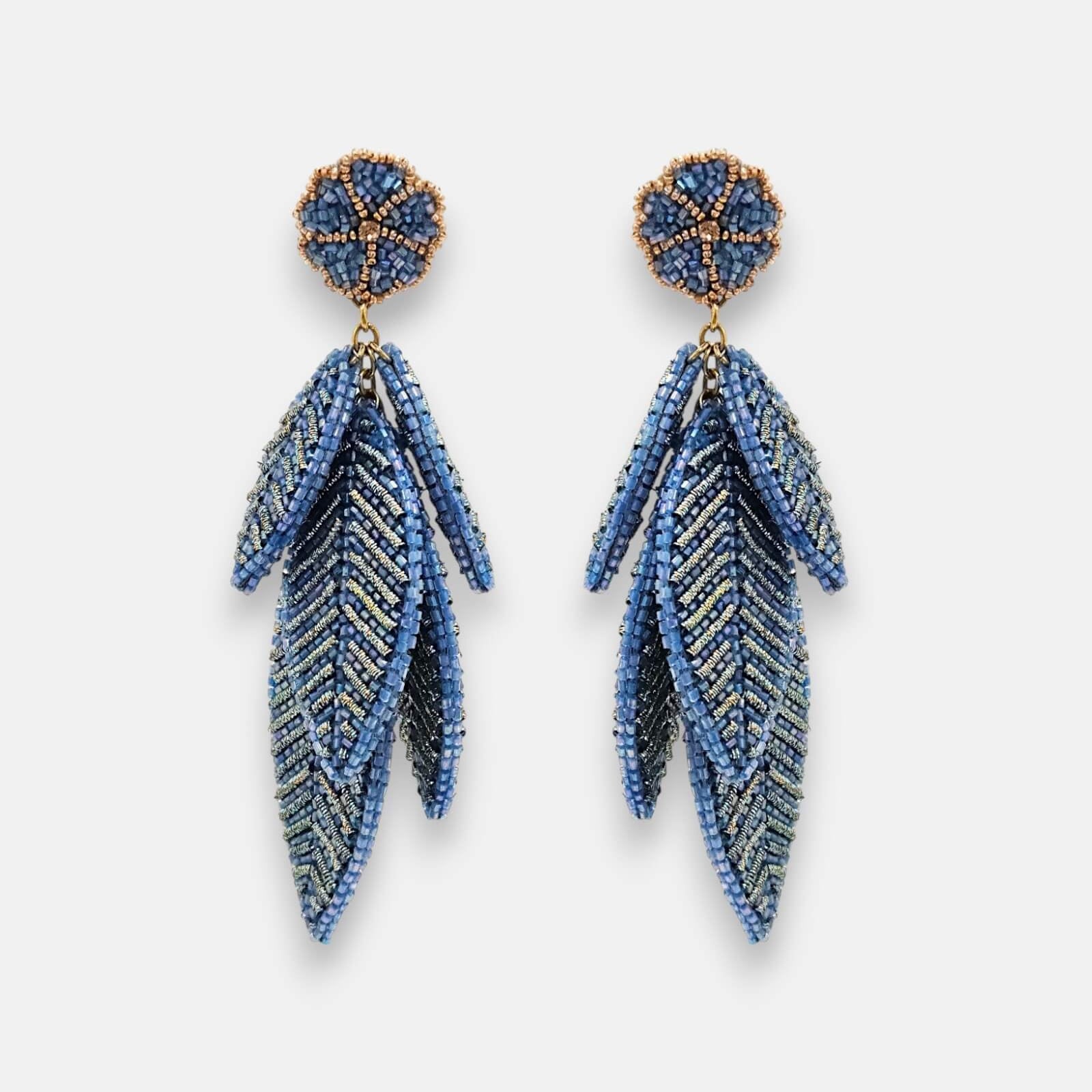 Pendientes "Bruma de Zafiro" con diseño de hojas escalonadas bordadas en hilos metálicos y cuentas azules sobre fondo claro.