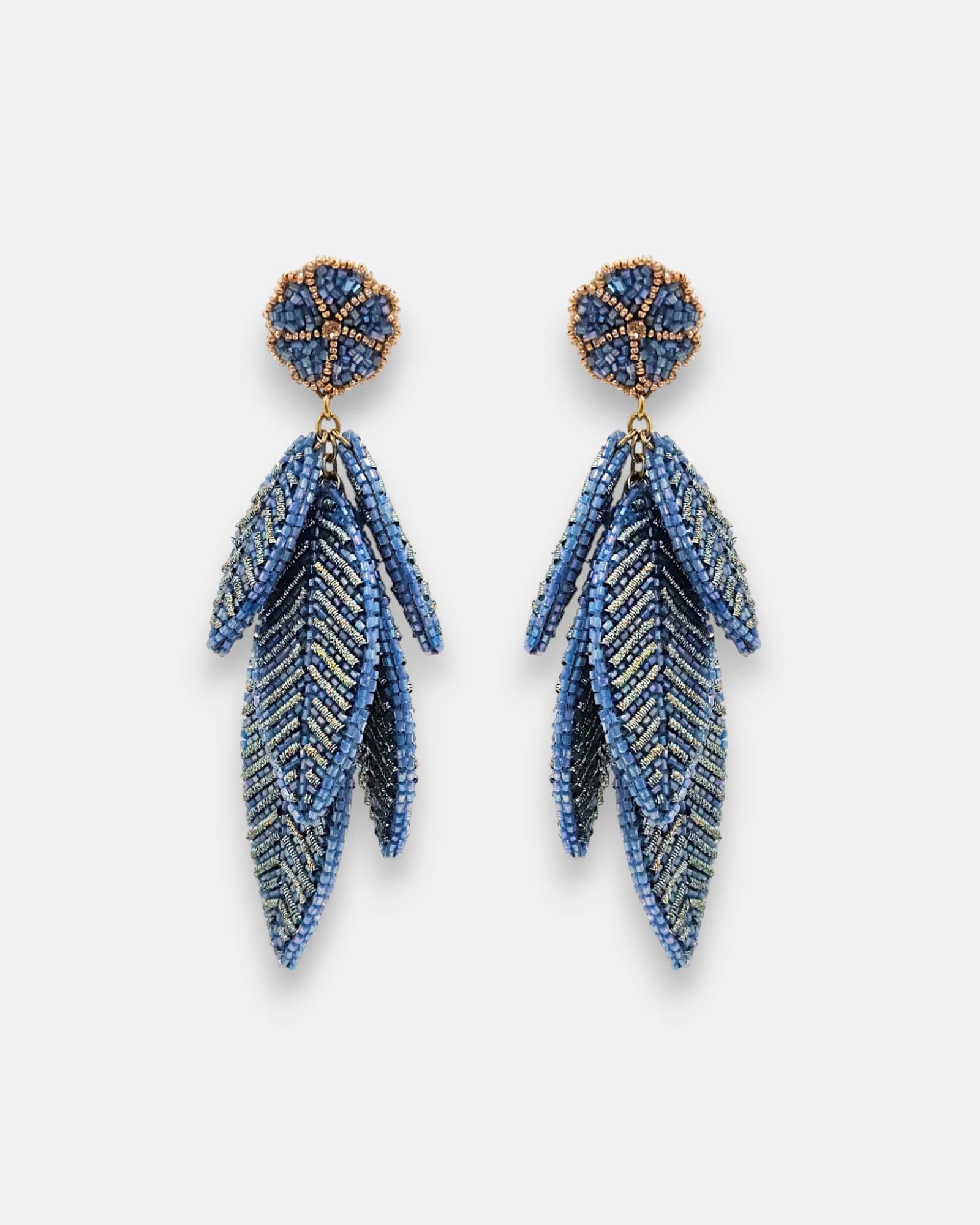 Pendientes "Bruma de Zafiro" con diseño de hojas escalonadas bordadas en hilos metálicos y cuentas azules sobre fondo claro.