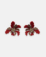 Par de pendientes "Flor de Fuego" de Gissa Bicalho con pétalos en resina roja y bronce con cristales centrales sobre fondo blanco.