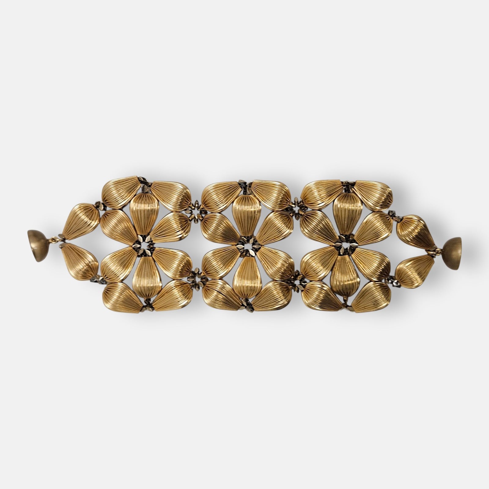 Maxi pulsera ancha Tataborello extendida con diseño calado de flores doradas estriadas y cierre magnético.