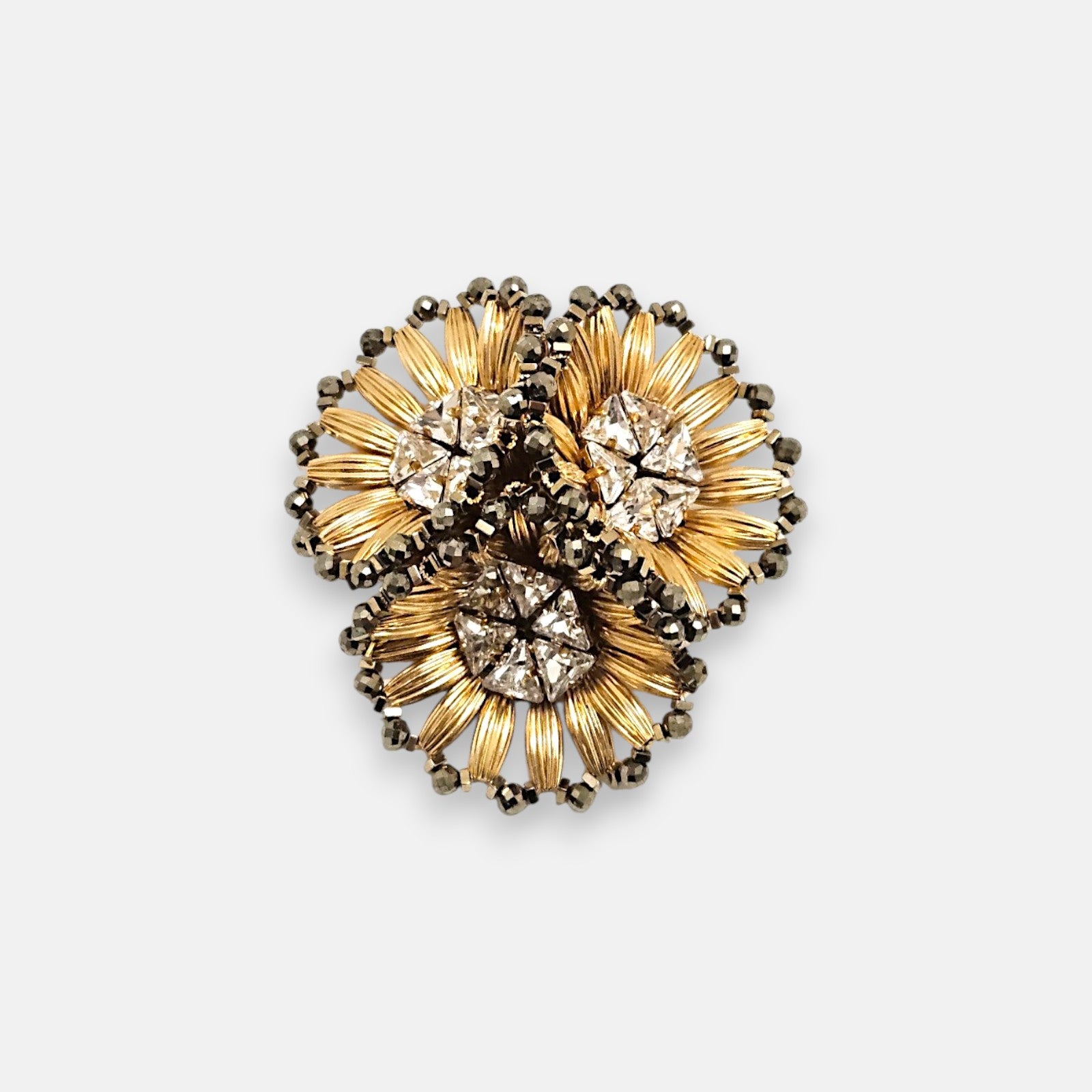 Broche de solapa maxi Tataborello compuesto por tres flores doradas estriadas con cristales en el centro.