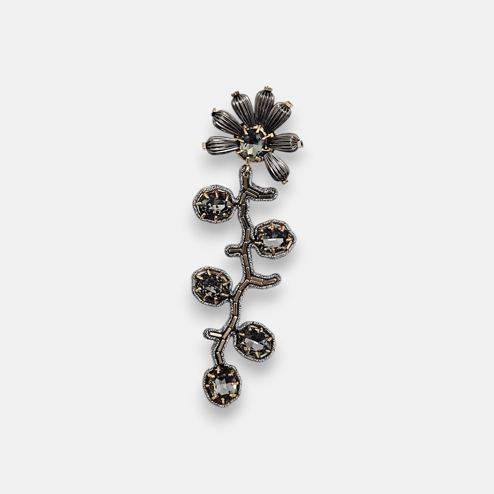 Pin broche vertical Tataborello con diseño de rama y flor en metal plateado oscuro con cristales facetados grises.