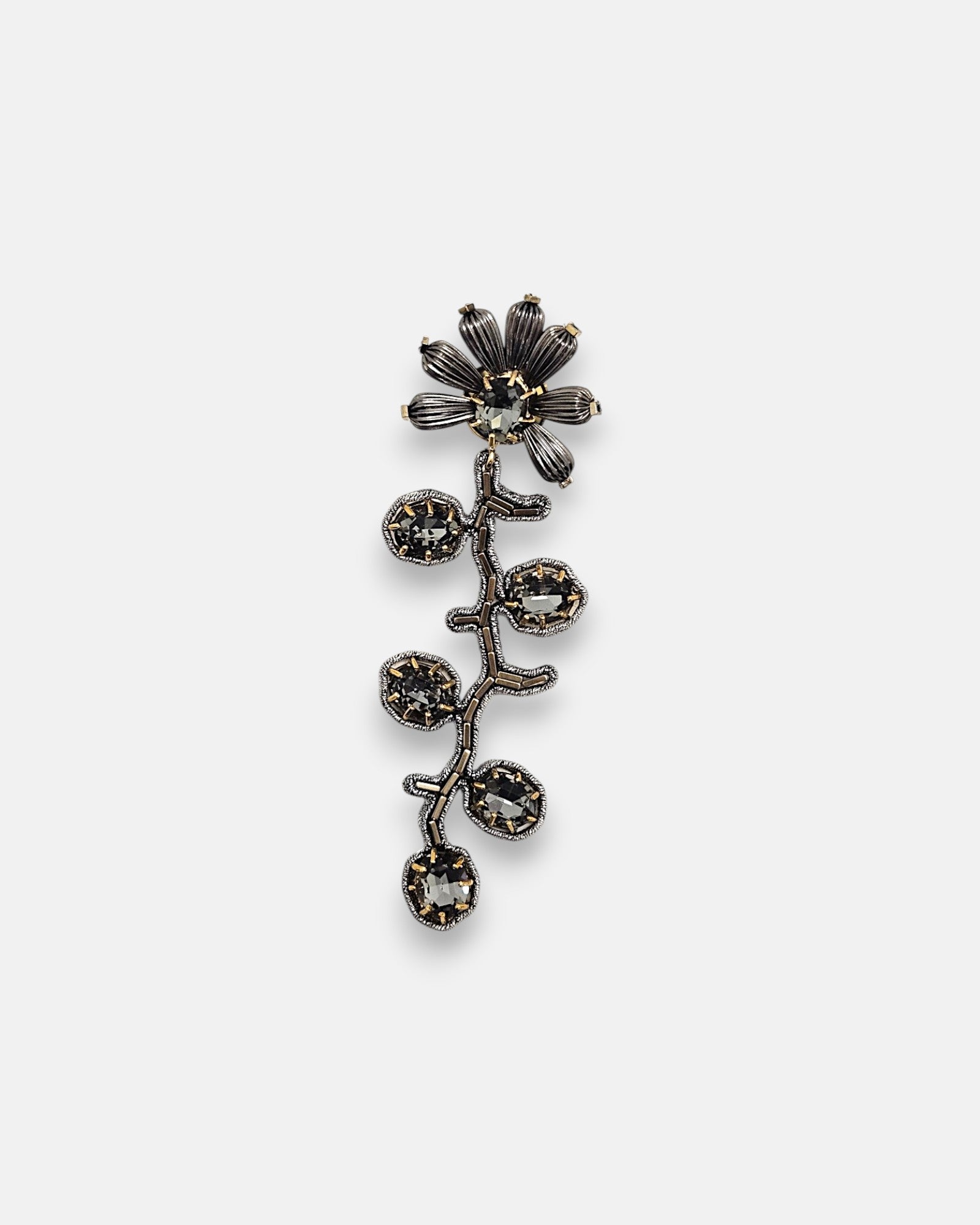 Pin broche vertical Tataborello con diseño de rama y flor en metal plateado oscuro con cristales facetados grises.