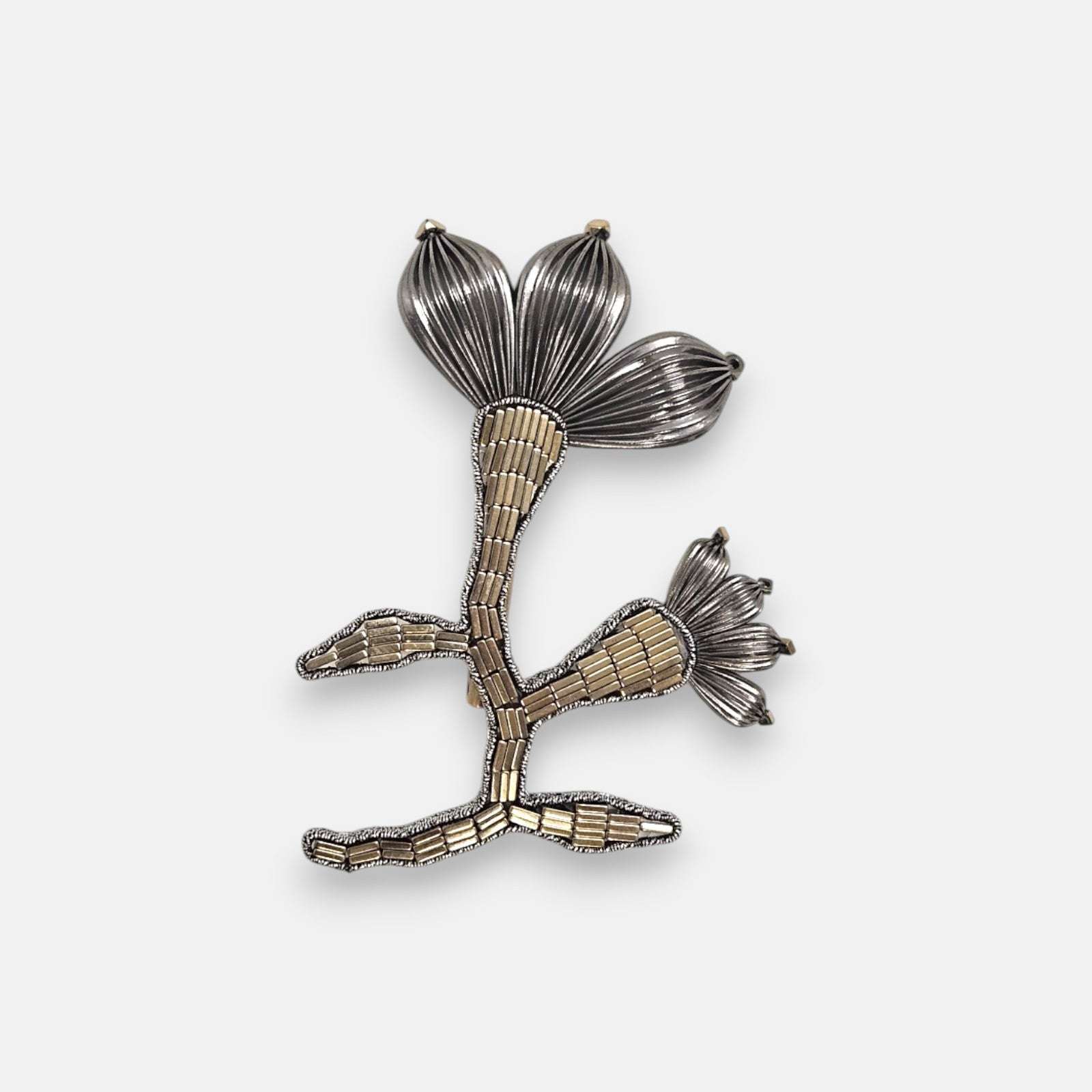 Broche artesanal de solapa Tataborello con silueta de flor y rama bordada en canutillos claros y pétalos estriados de rutenio oscuro.