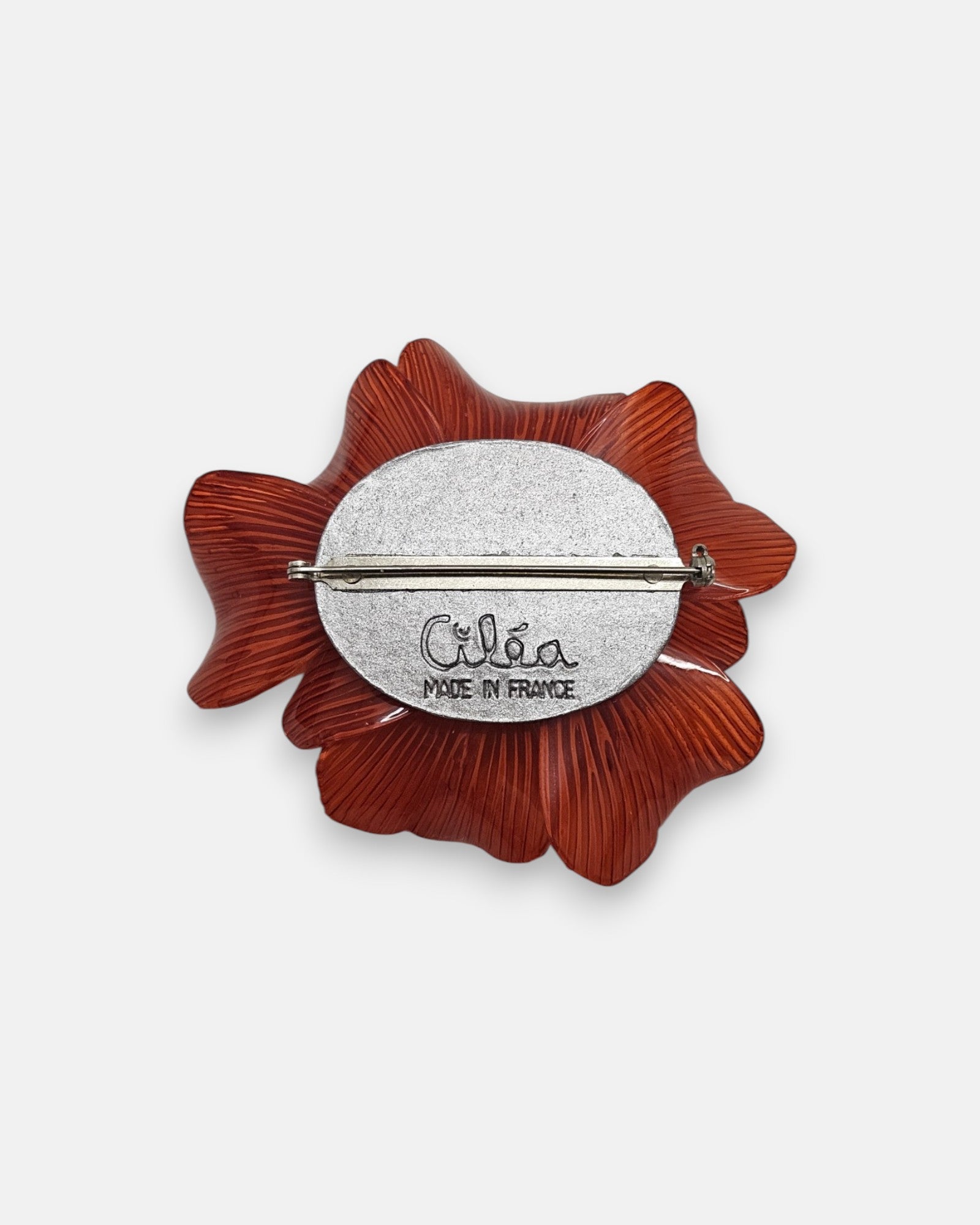 reverso del broche artesanal, detallando la base circular metálica con el pasador de aguja y la firma oficial grabada "Ciléa Made in France".