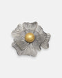 broche con forma de flor de Ciléa Paris sobre fondo neutro, apreciando su juego de capas estriadas plateadas y el centro de color oro.