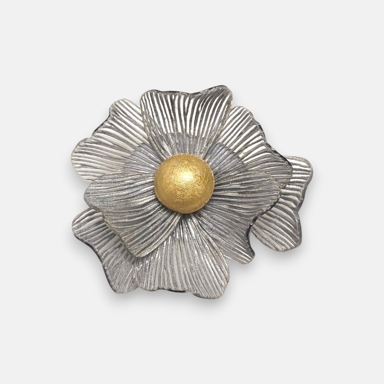 broche con forma de flor de Ciléa Paris sobre fondo neutro, apreciando su juego de capas estriadas plateadas y el centro de color oro.