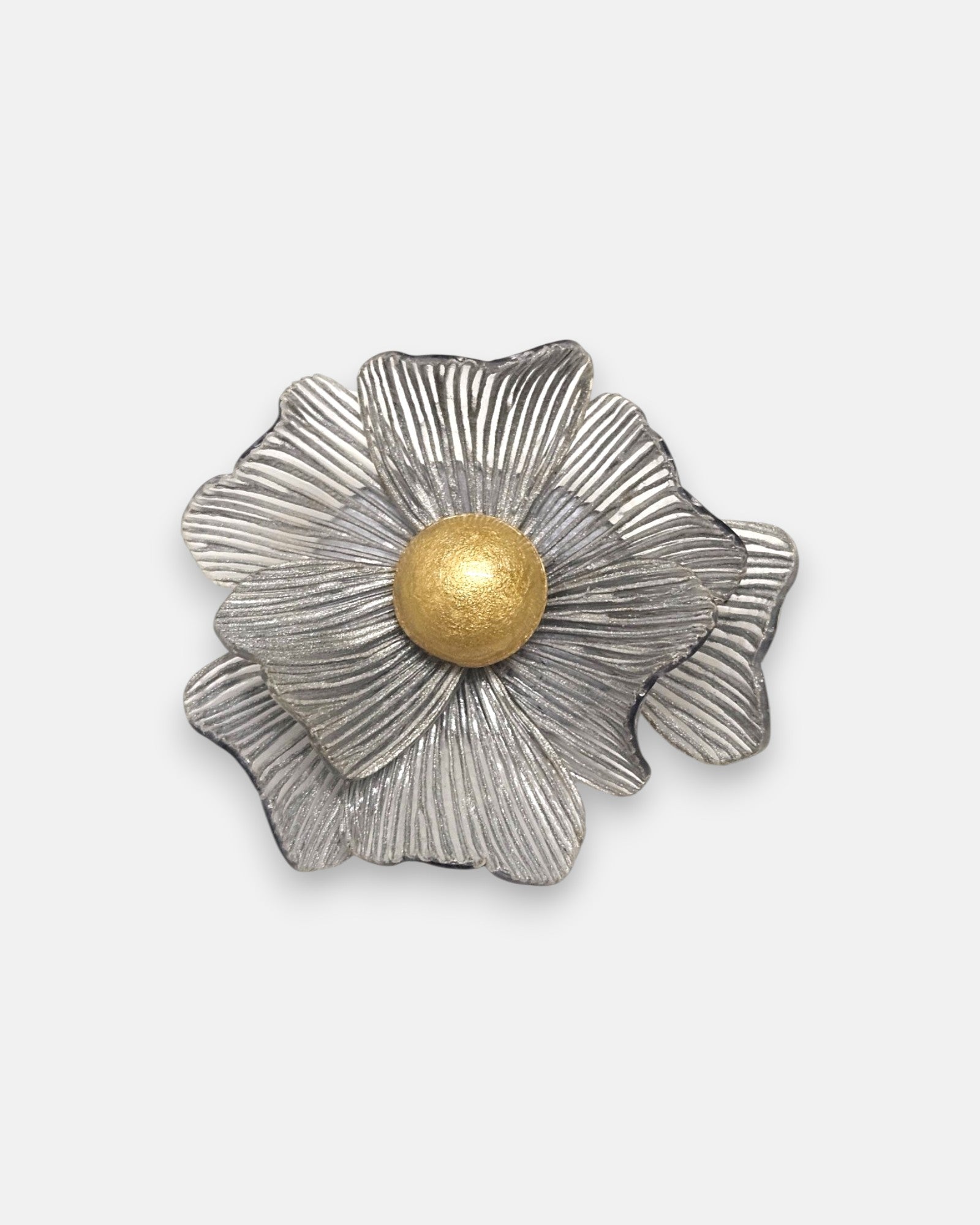 broche con forma de flor de Ciléa Paris sobre fondo neutro, apreciando su juego de capas estriadas plateadas y el centro de color oro.