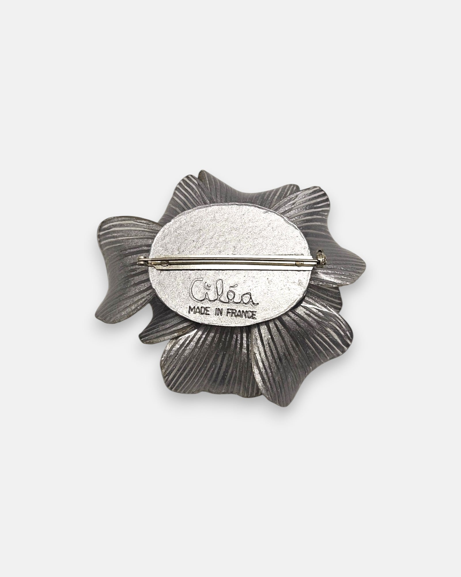 reverso del broche artesanal, detallando el pasador metálico de aguja para la sujeción y la firma labrada de la marca "Ciléa Made in France".