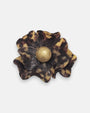 broche de flor de Ciléa Paris sobre fondo neutro, apreciando su diseño de pétalos estriados con patrón de carey en marrón y negro con centro dorado.