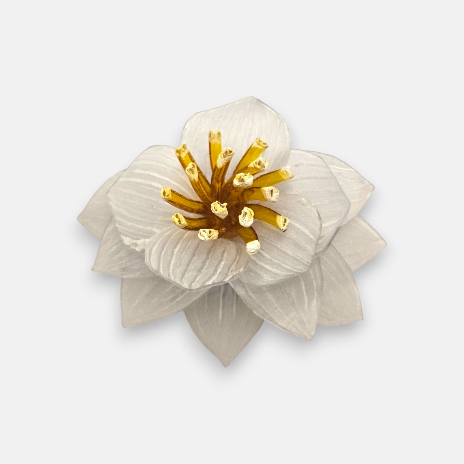 broche de loto blanco de frente en primer plano sobre fondo neutro, detallando sus pétalos estriados translúcidos y el centro con pistilos color ámbar.