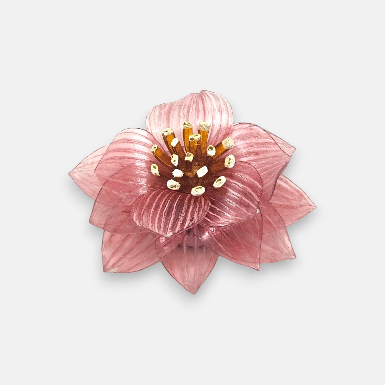 broche de flor de loto de Ciléa Paris sobre fondo claro, apreciando su juego de capas de pétalos estriados color rosa viejo y su centro ámbar.