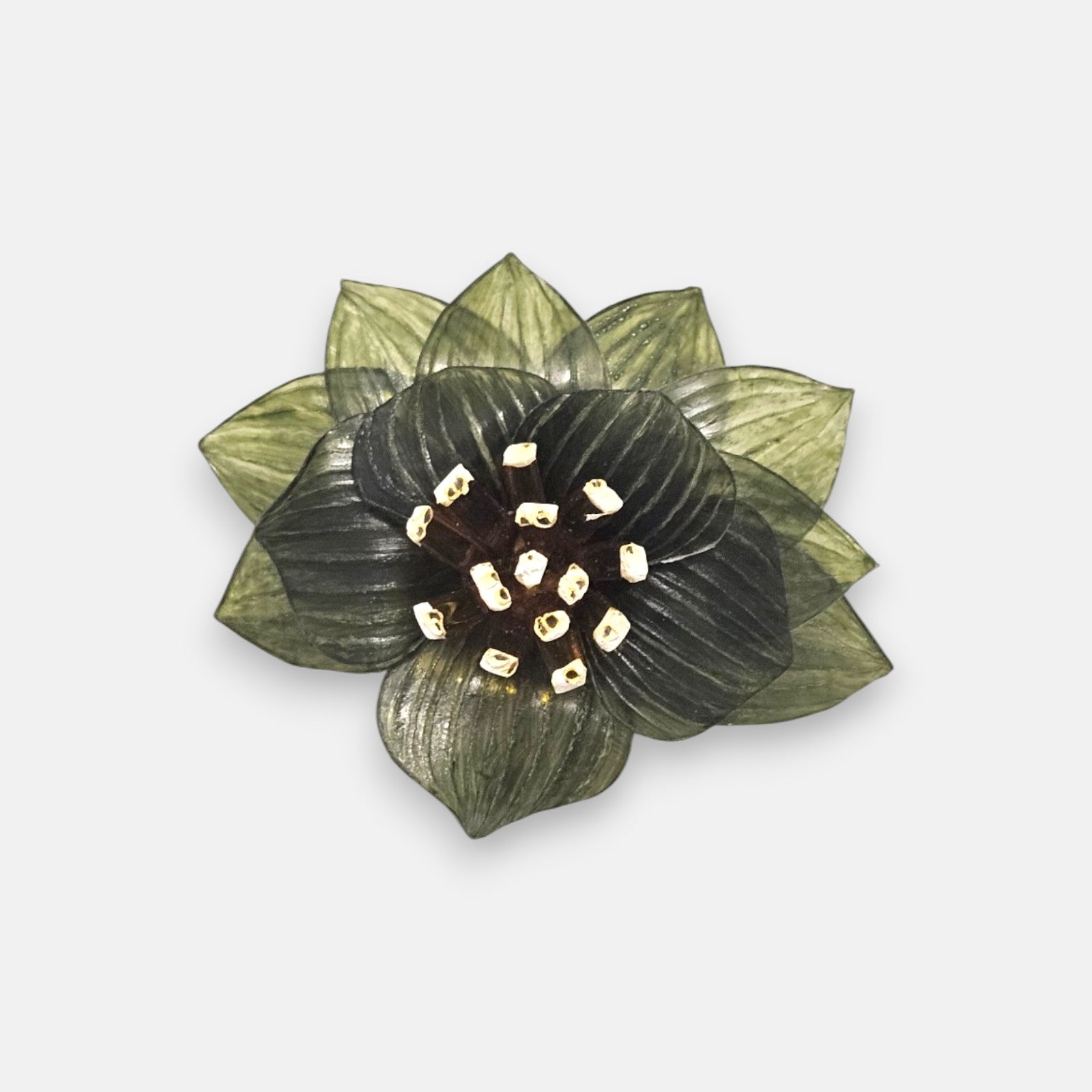 broche con forma de flor de loto de Ciléa Paris sobre fondo claro, apreciando la disposición de sus capas en resina translúcida verde oliva y su centro de pistilos.