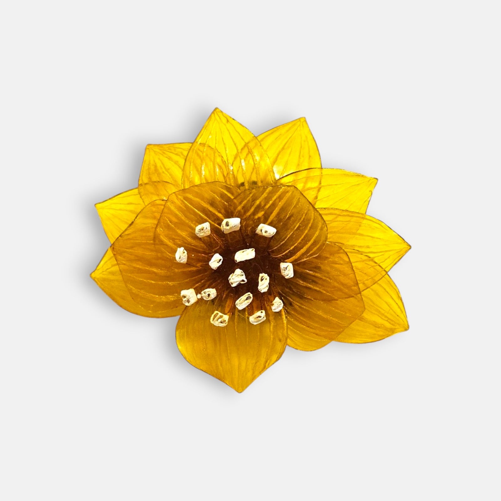 broche con forma de flor de loto de Ciléa Paris sobre fondo claro, apreciando su diseño de pétalos estriados en resina translúcida de color amarillo mostaza.