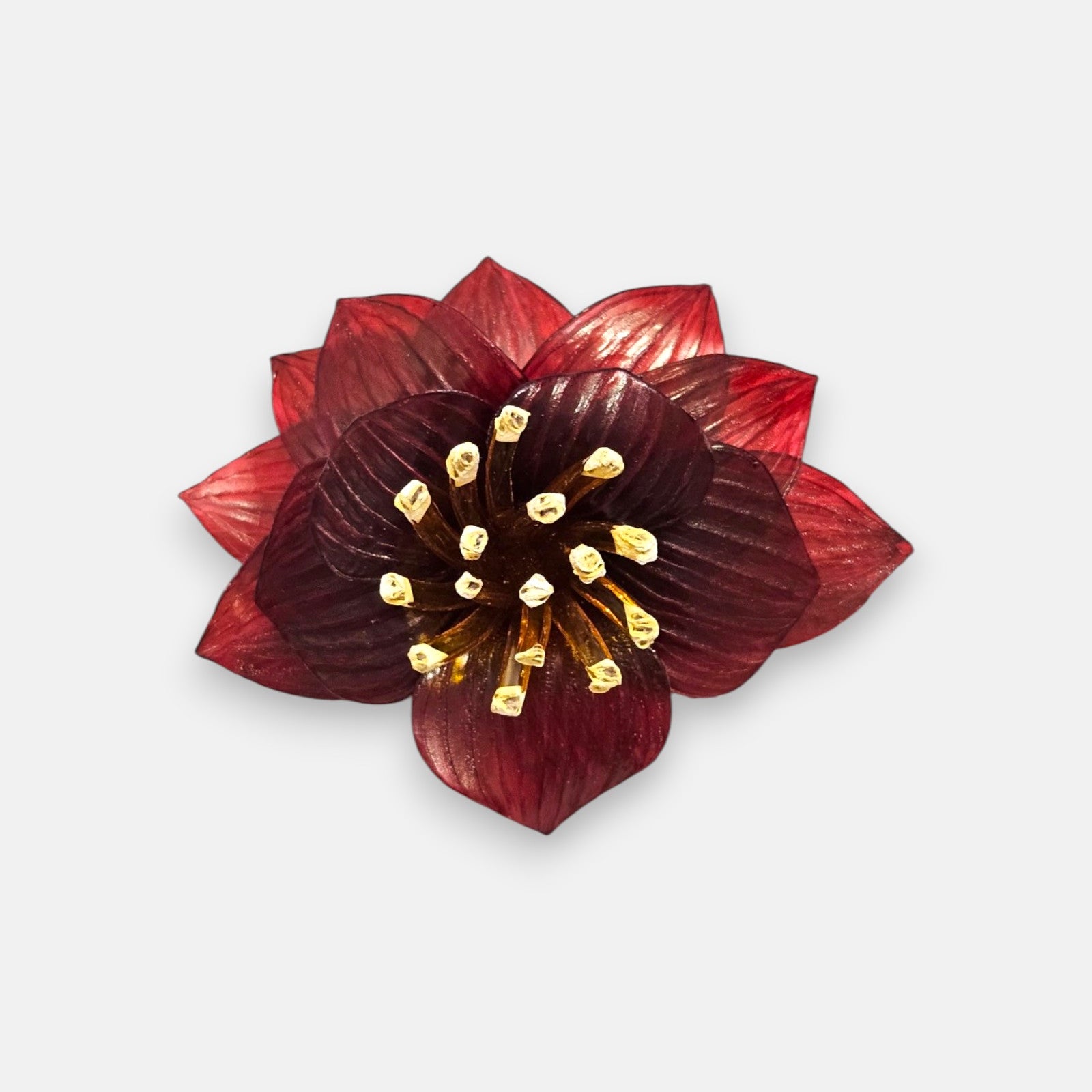 broche con forma de flor de loto de Ciléa Paris sobre fondo claro, apreciando la disposición de sus capas en resina translúcida de color rojo y su centro de pistilos.