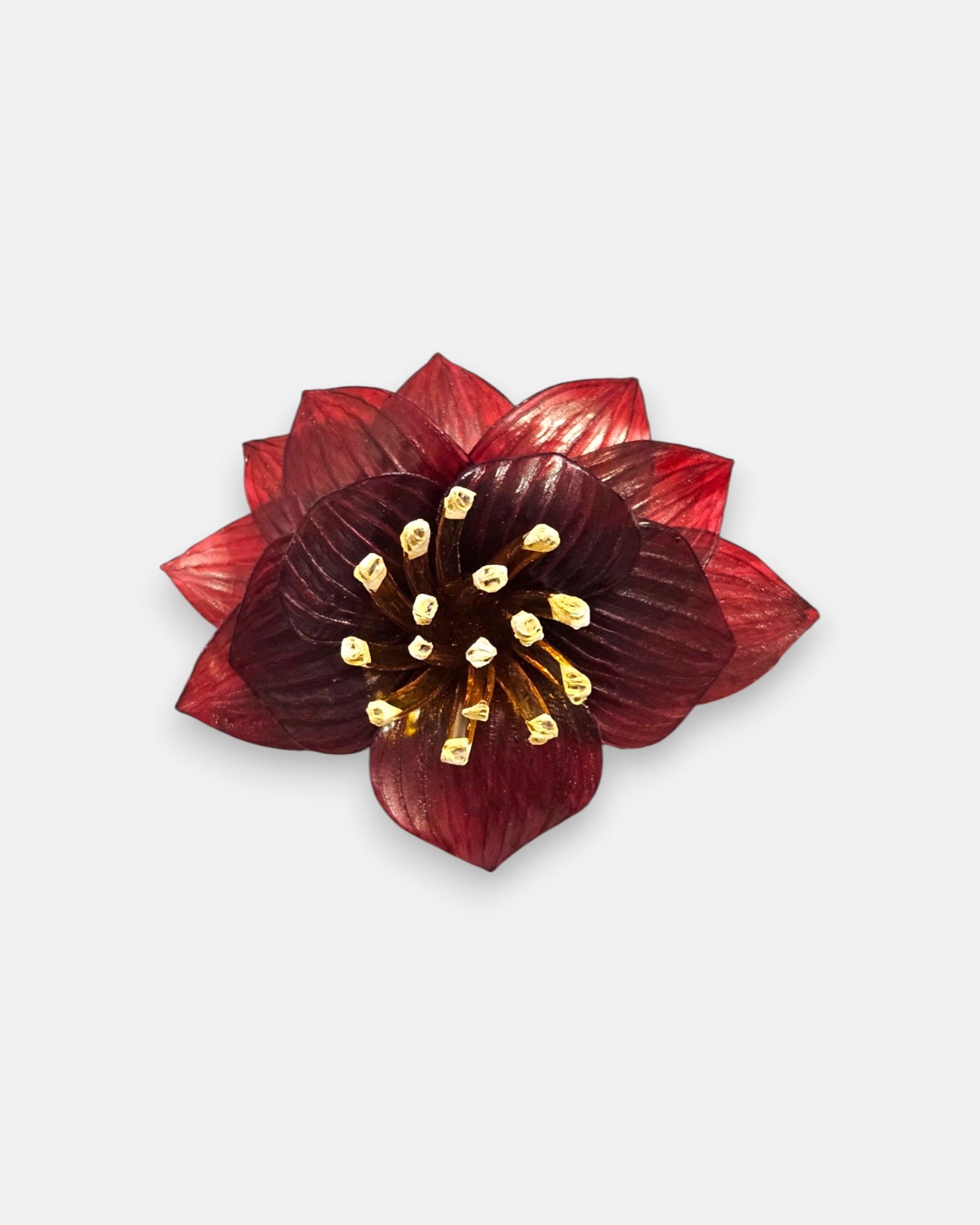 broche con forma de flor de loto de Ciléa Paris sobre fondo claro, apreciando la disposición de sus capas en resina translúcida de color rojo y su centro de pistilos.