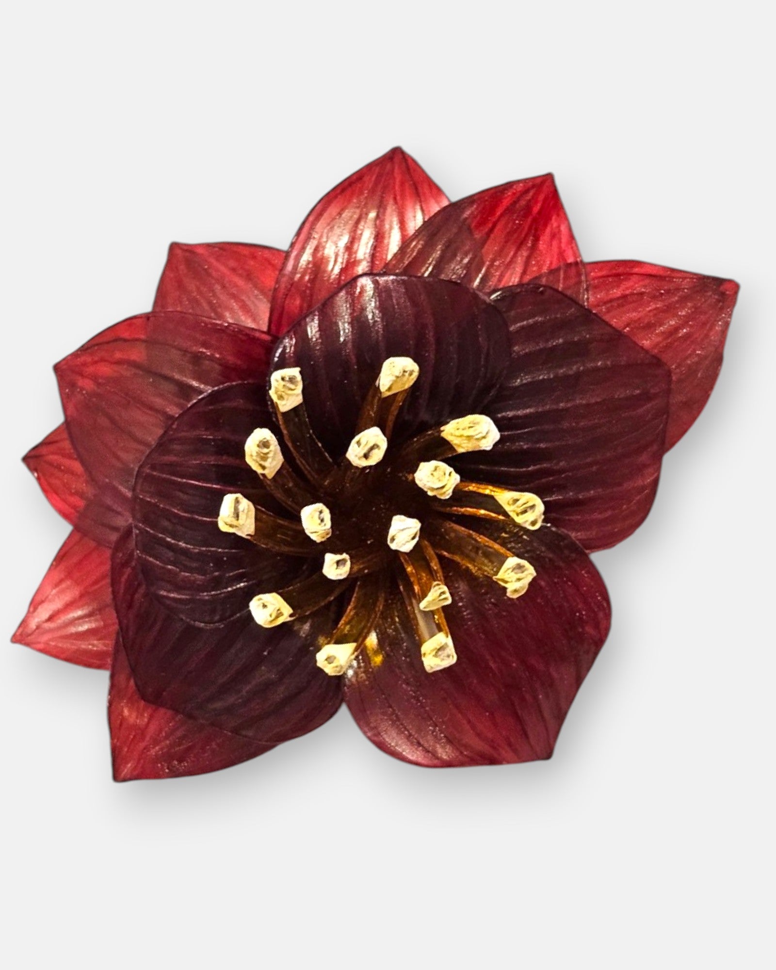 plano macro del broche floral, resaltando las sutiles líneas grabadas en los pétalos rojos y la textura tridimensional de los elementos centrales.