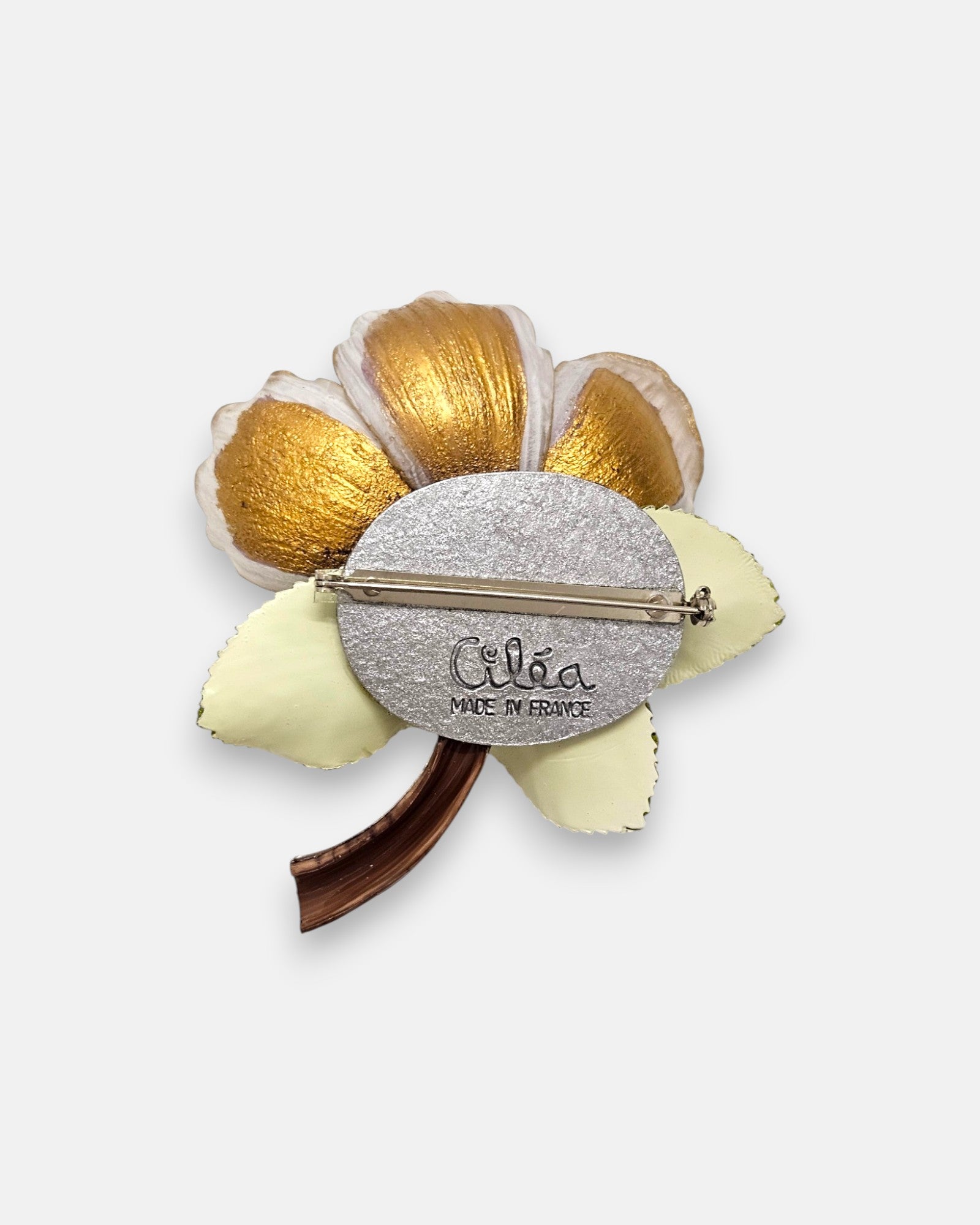 reverso de la pieza de autor, detallando el pasador metálico de aguja para la sujeción, la placa circular plateada y el sello oficial grabado "Ciléa Made in France".