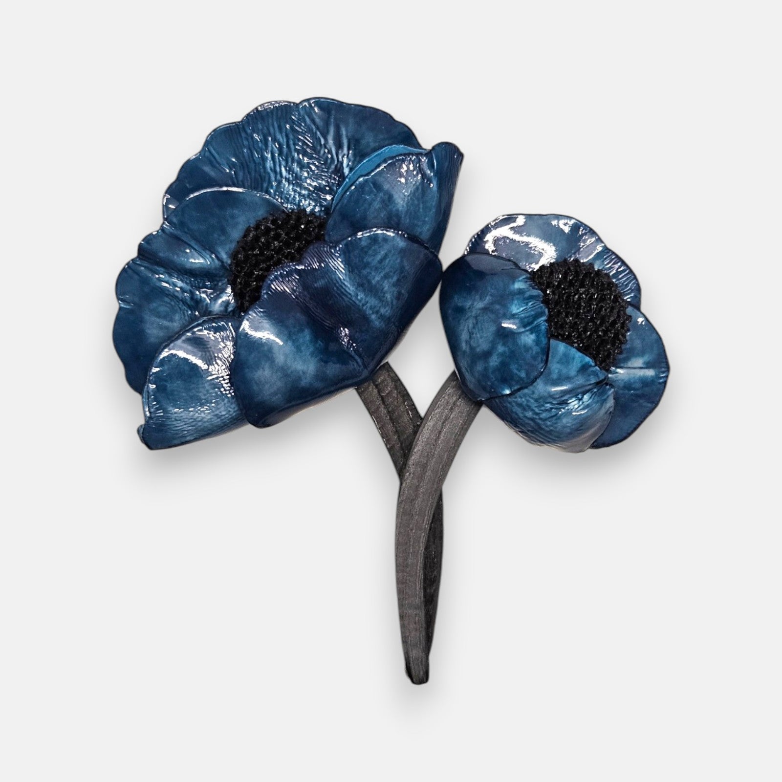 broche de doble flor de Ciléa Paris sobre fondo claro, apreciando el acabado brillante de sus pétalos azul índigo con centros negros y tallos entrelazados.