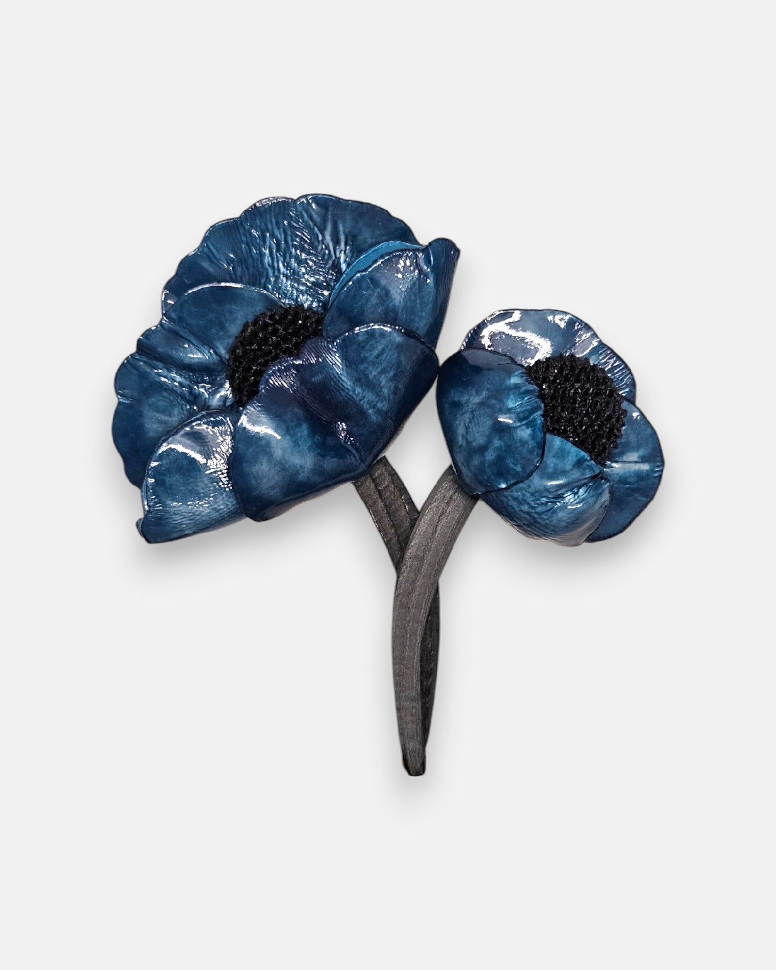 broche de doble flor de Ciléa Paris sobre fondo claro, apreciando el acabado brillante de sus pétalos azul índigo con centros negros y tallos entrelazados.