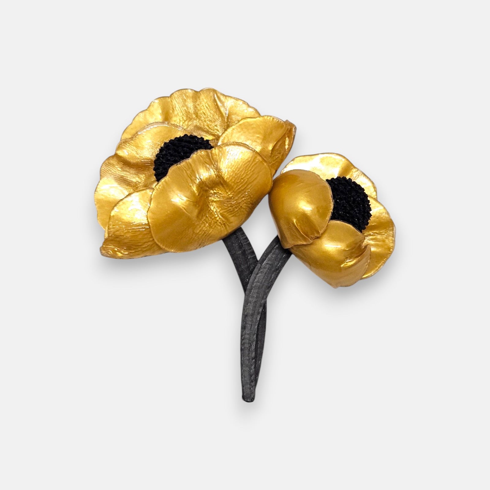 broche de doble flor de Ciléa Paris sobre fondo claro, apreciando el acabado satinado de sus pétalos dorados con centros negros y tallos entrelazados.
