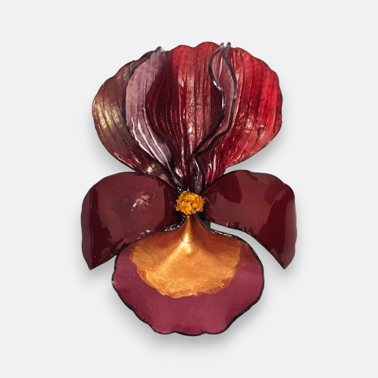 broche con forma de flor de iris sobre fondo neutro, destacando sus pétalos superiores estriados en color carmín y su base en tonos granate y oro satinado.