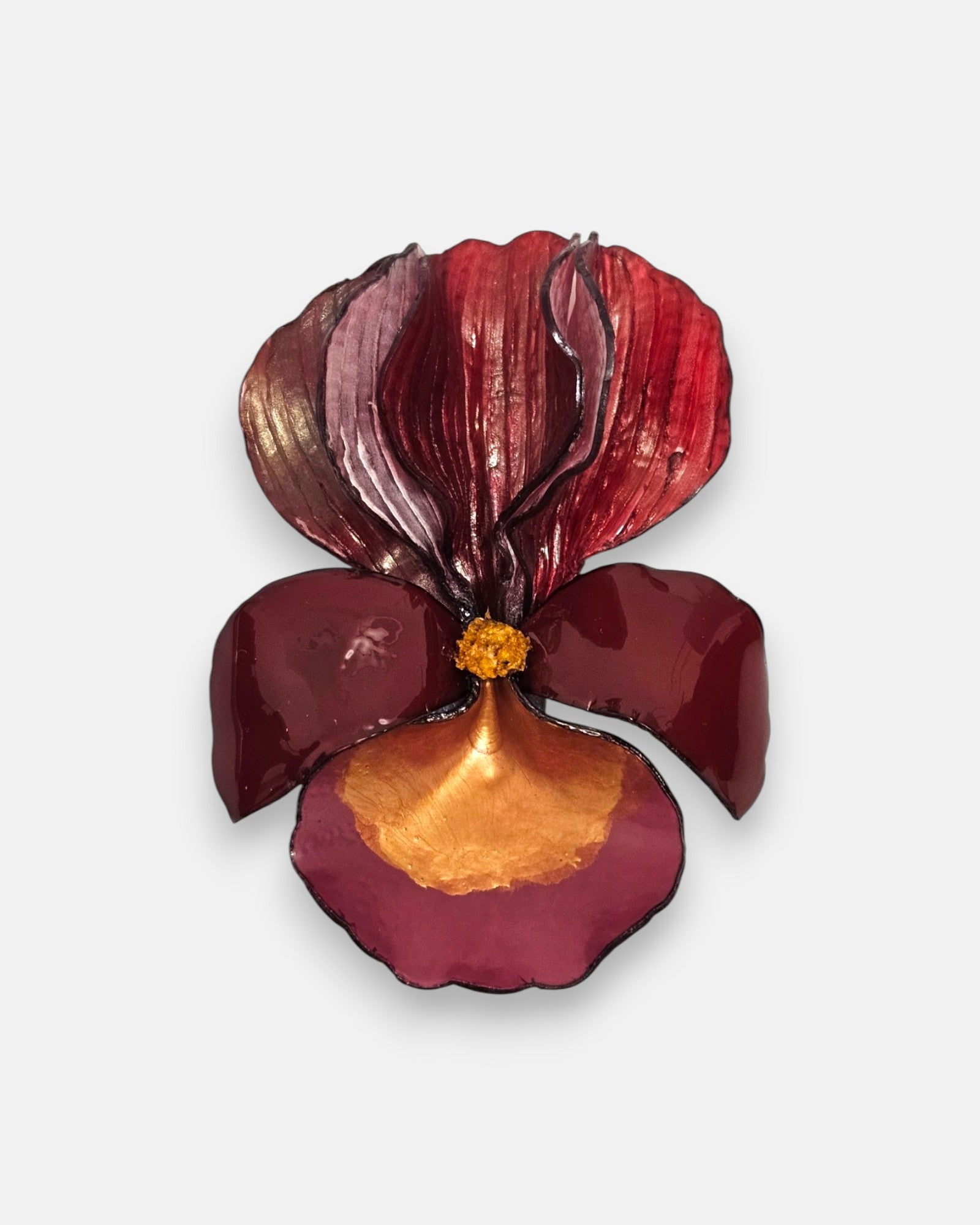 broche con forma de flor de iris sobre fondo neutro, destacando sus pétalos superiores estriados en color carmín y su base en tonos granate y oro satinado.