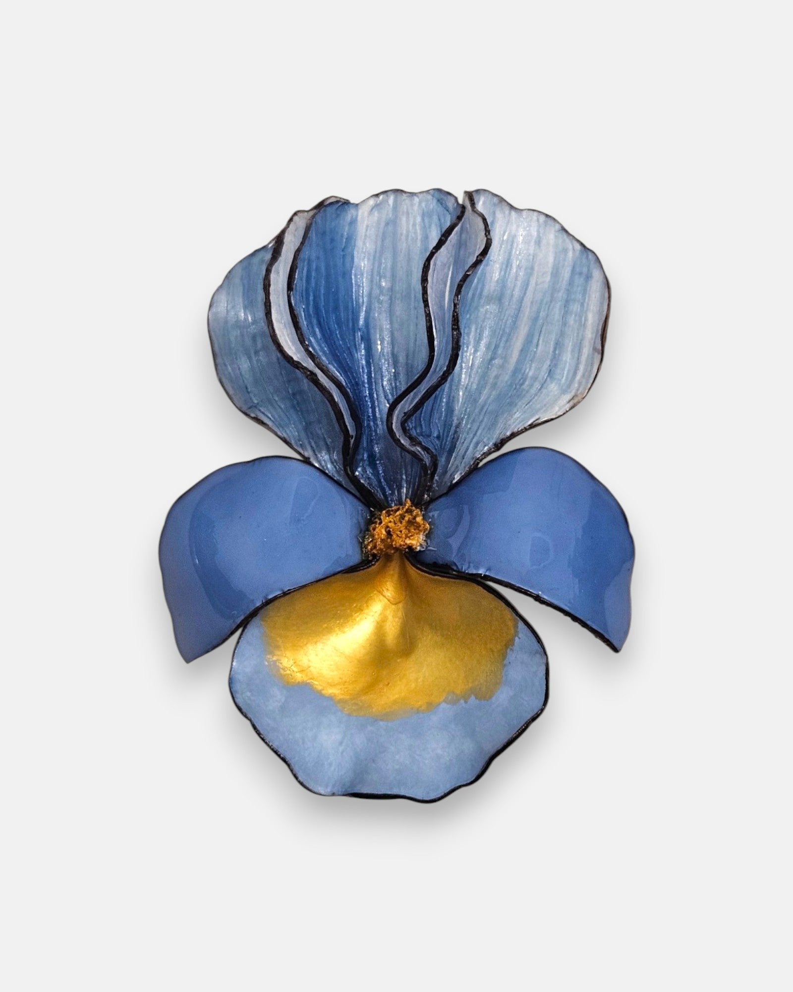 broche con forma de flor de iris sobre fondo neutro, destacando sus pétalos superiores en azul degradado y su base en tonos azul cerúleo y oro satinado.