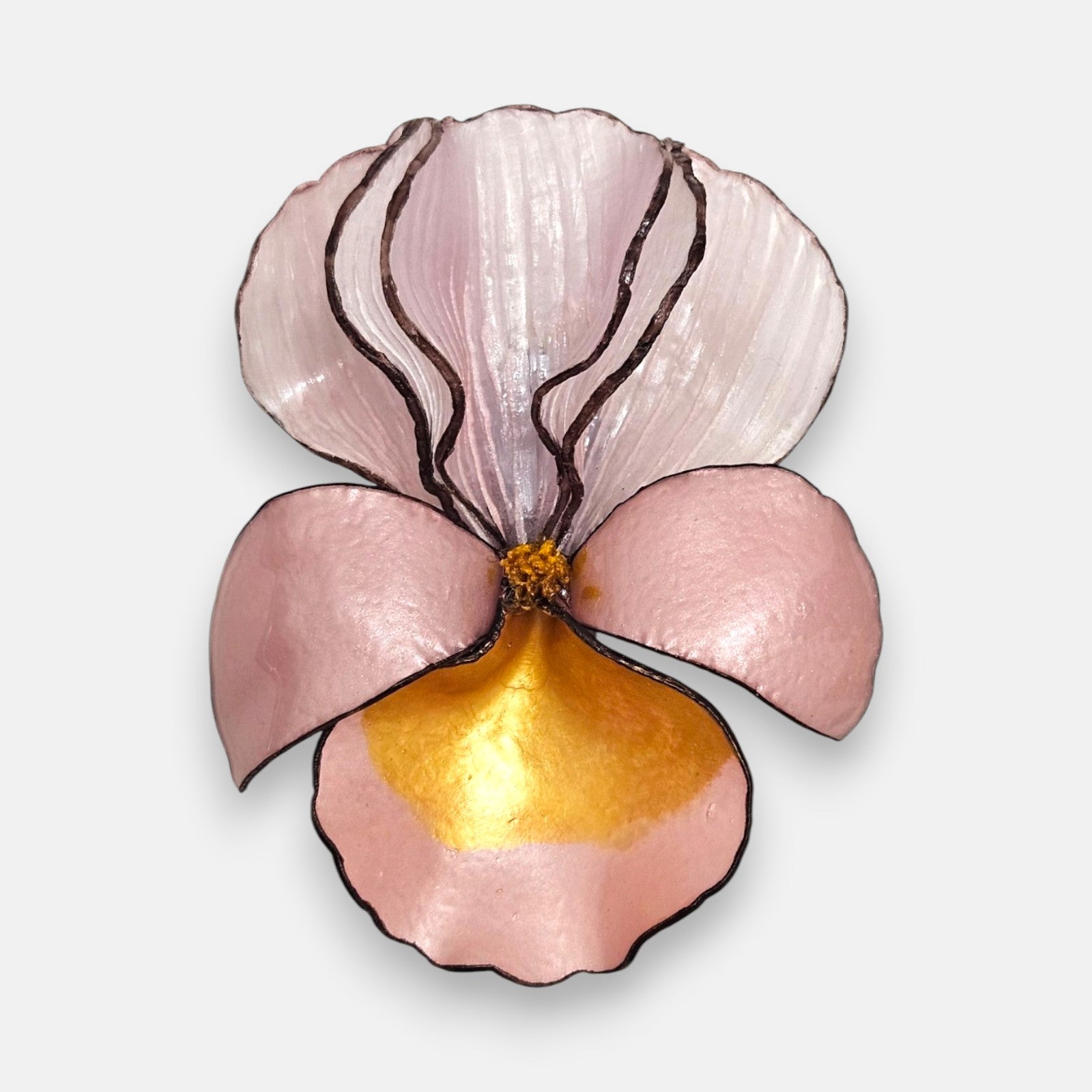 broche con forma de flor de iris sobre fondo neutro, destacando sus pétalos superiores en rosa nácar translúcido y su base en tonos rosa pastel y oro satinado.