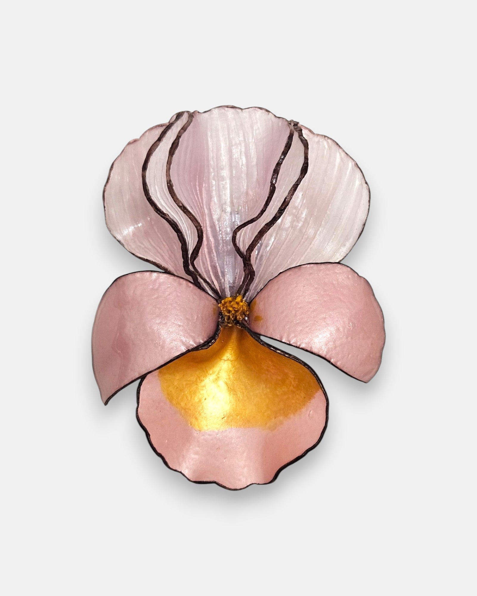 broche con forma de flor de iris sobre fondo neutro, destacando sus pétalos superiores en rosa nácar translúcido y su base en tonos rosa pastel y oro satinado.