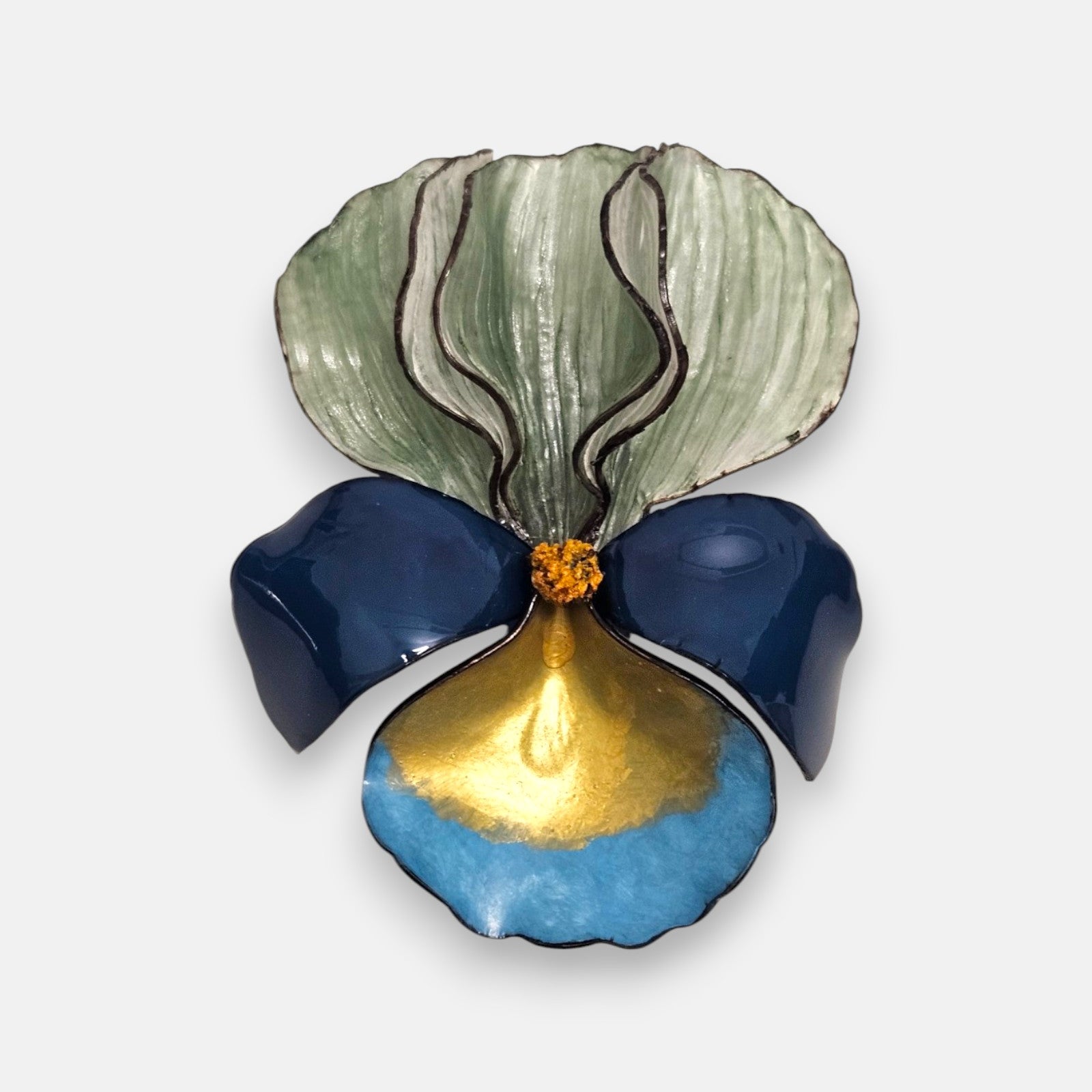 broche con forma de flor de iris sobre fondo neutro, destacando sus pétalos superiores en verde menta degradado y su base en tonos azul marino, turquesa y oro satinado.