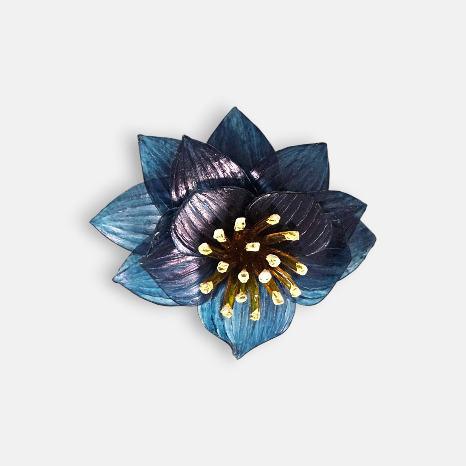 broche con forma de flor de loto de Ciléa Paris sobre fondo claro, apreciando la disposición de sus capas en resina translúcida de color azul y su centro de pistilos.