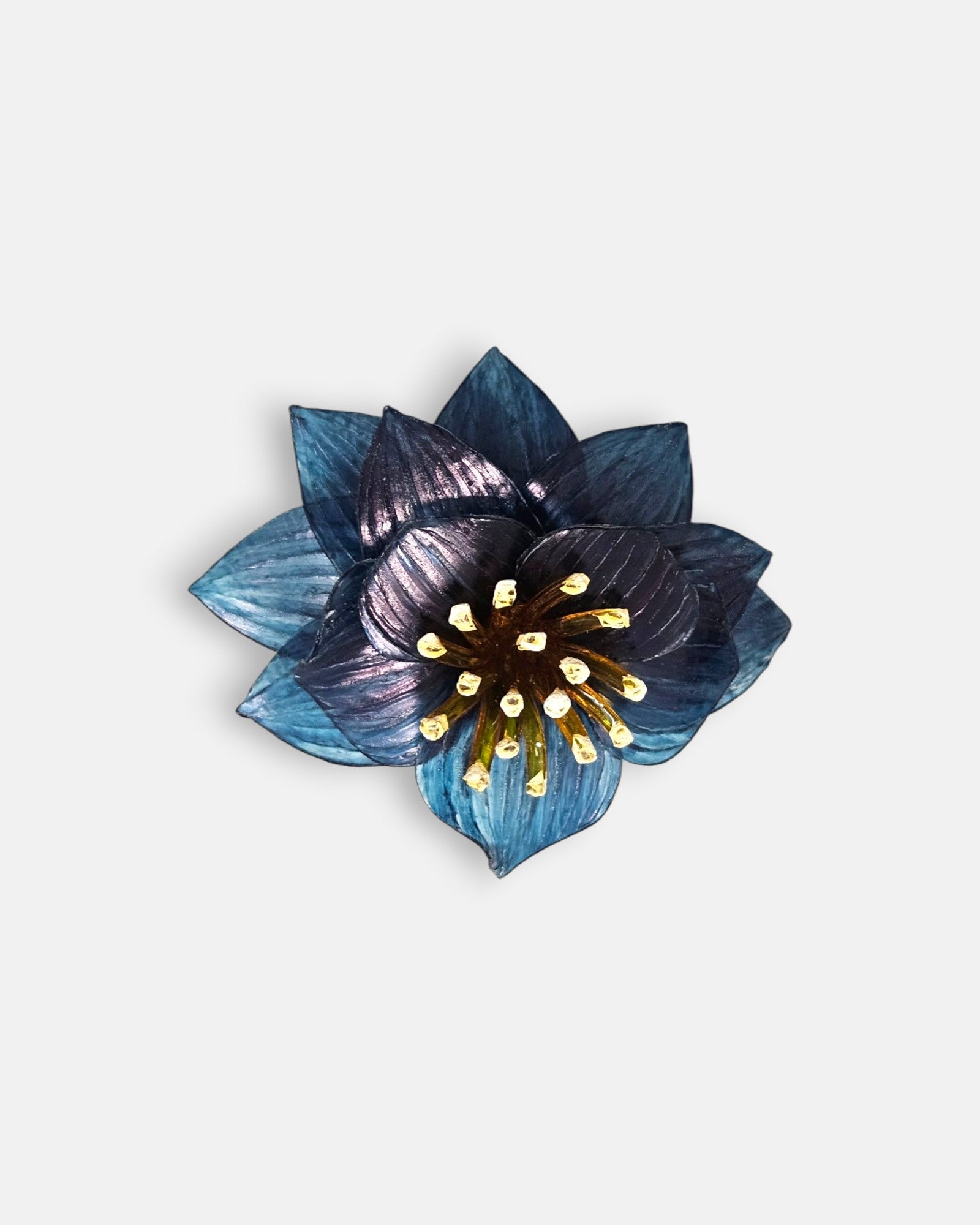 broche con forma de flor de loto de Ciléa Paris sobre fondo claro, apreciando la disposición de sus capas en resina translúcida de color azul y su centro de pistilos.