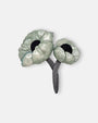 broche de doble flor de Ciléa Paris sobre fondo claro, apreciando el acabado brillante de sus pétalos verde menta con centros negros y tallos entrelazados.
