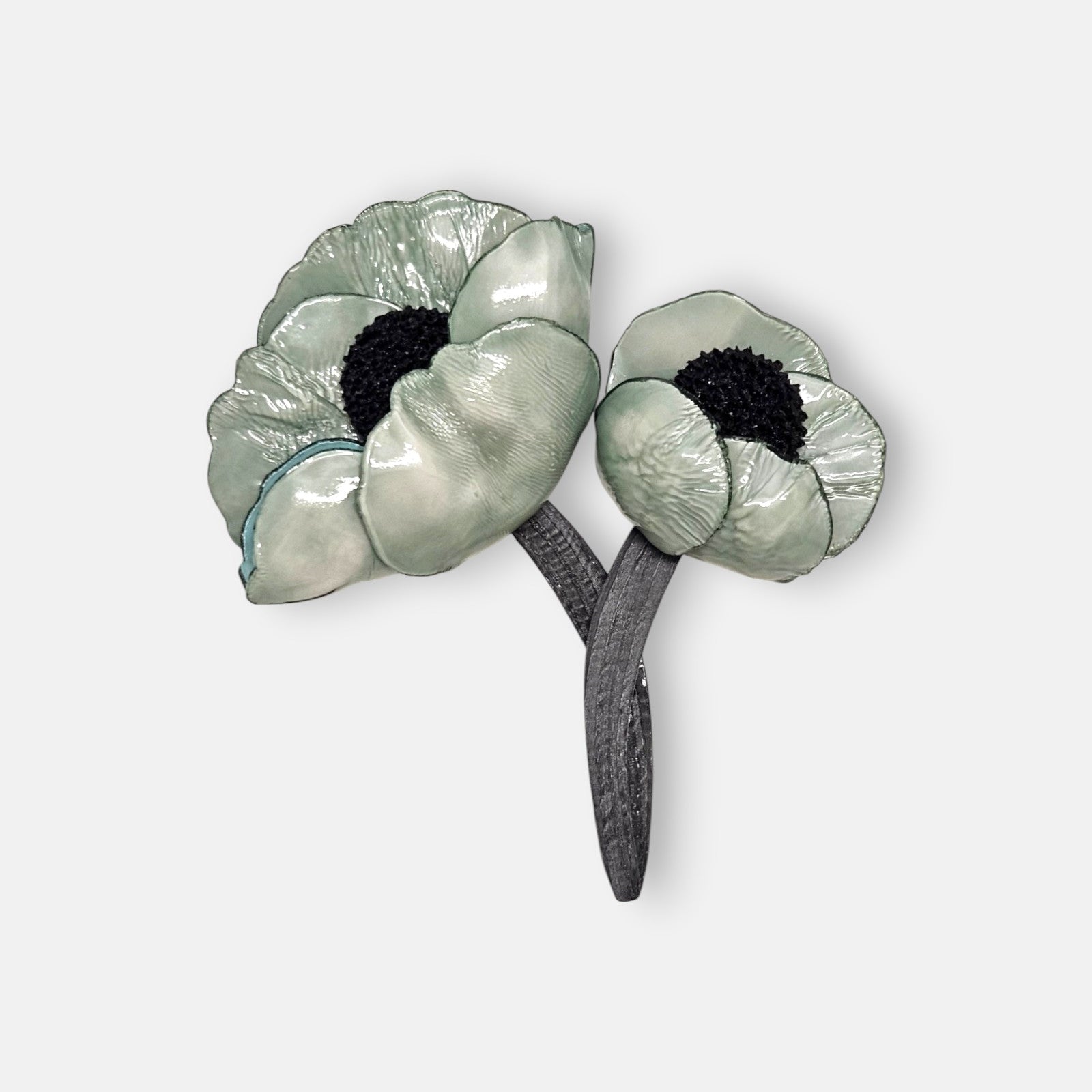 broche de doble flor de Ciléa Paris sobre fondo claro, apreciando el acabado brillante de sus pétalos verde menta con centros negros y tallos entrelazados.