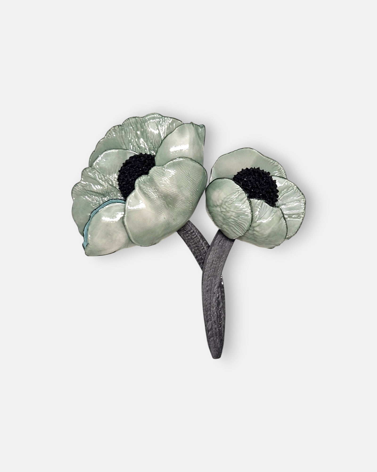 broche de doble flor de Ciléa Paris sobre fondo claro, apreciando el acabado brillante de sus pétalos verde menta con centros negros y tallos entrelazados.
