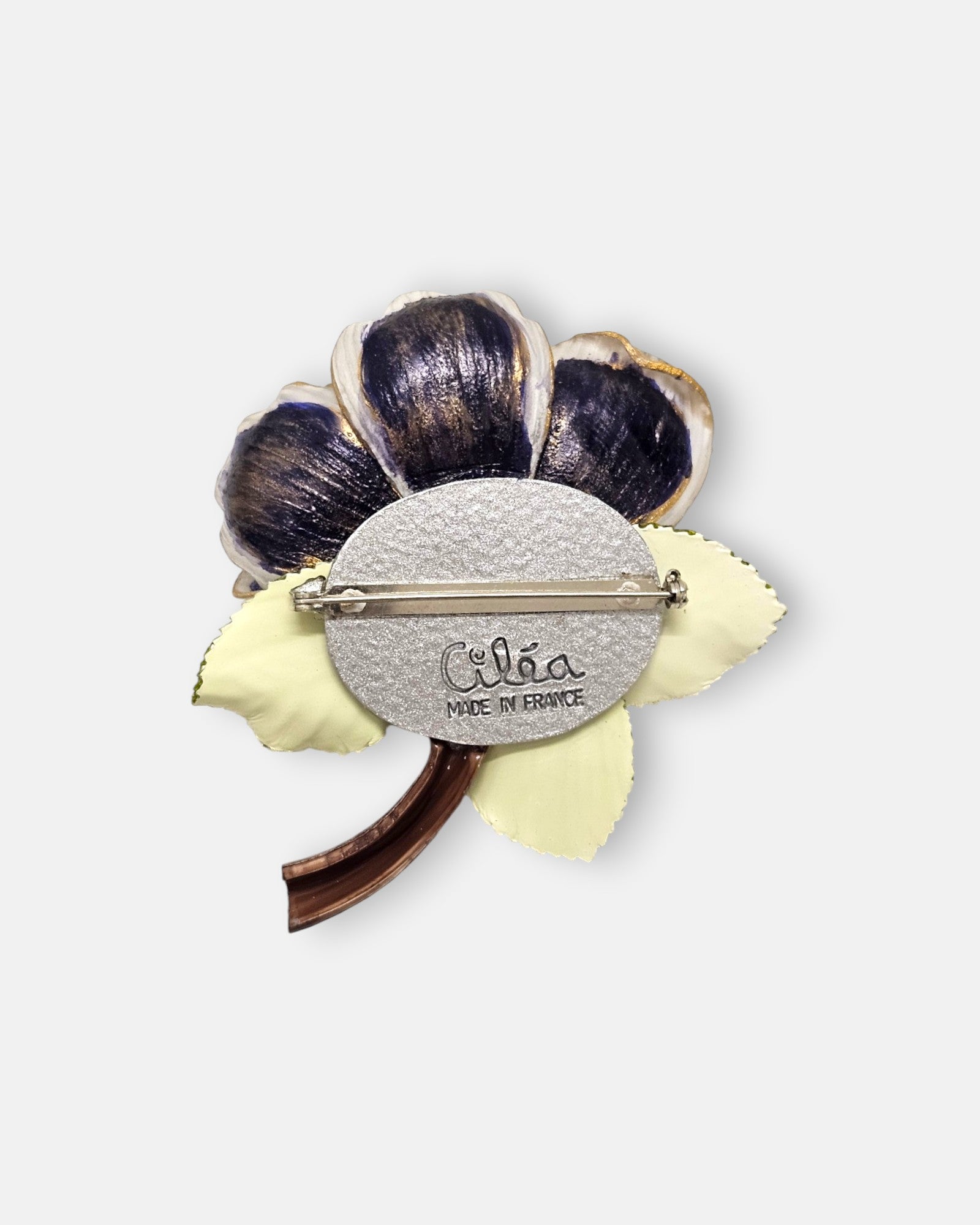 reverso de la pieza de autor, detallando el pasador metálico de aguja para la sujeción, la placa circular plateada y el sello oficial grabado "Ciléa Made in France".