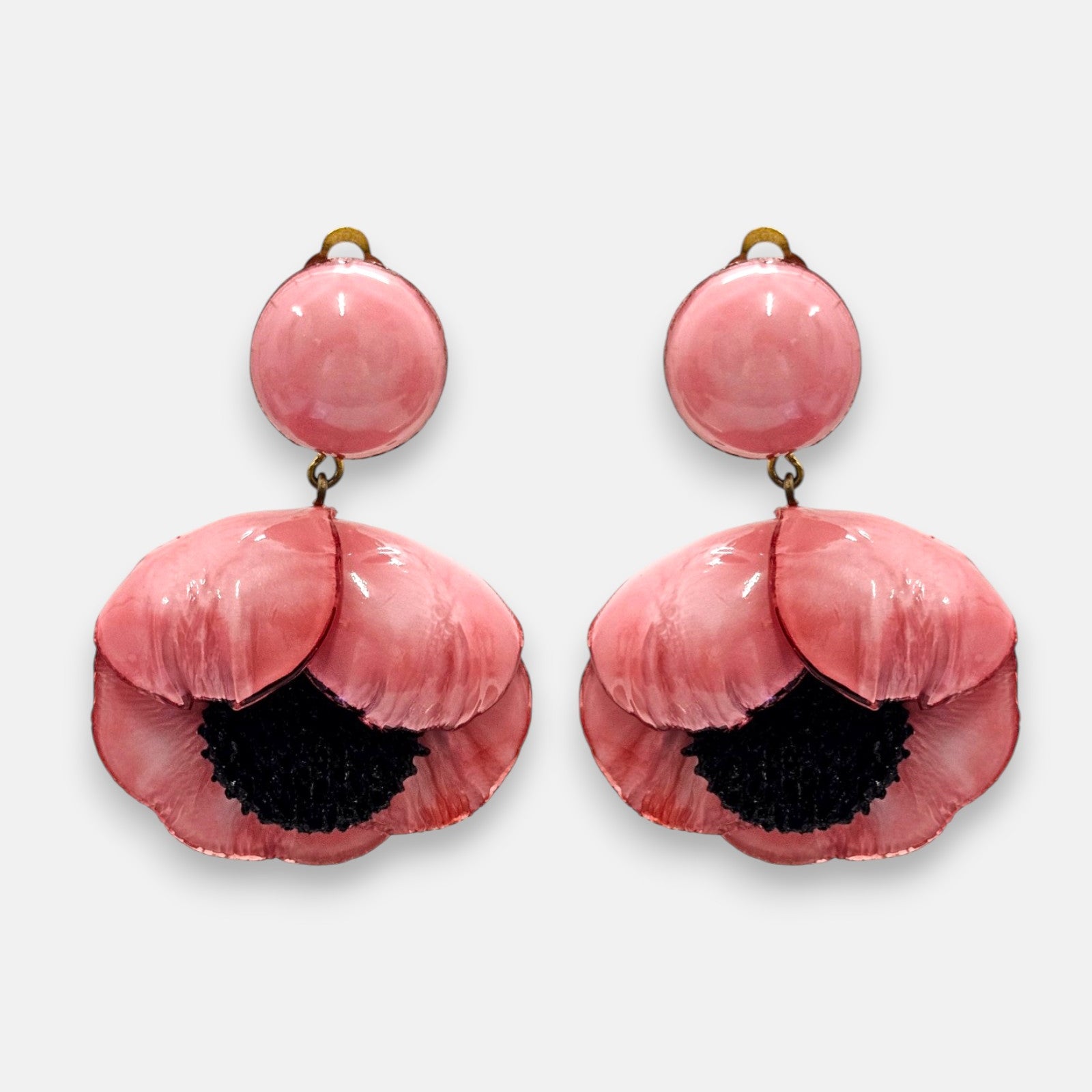 par de pendientes de clip con forma de flor de amapola de Ciléa Paris, detallando su botón superior redondo con la pequeña pestaña del cierre de pinza asomando y sus pétalos rosa chicle con centro negro.