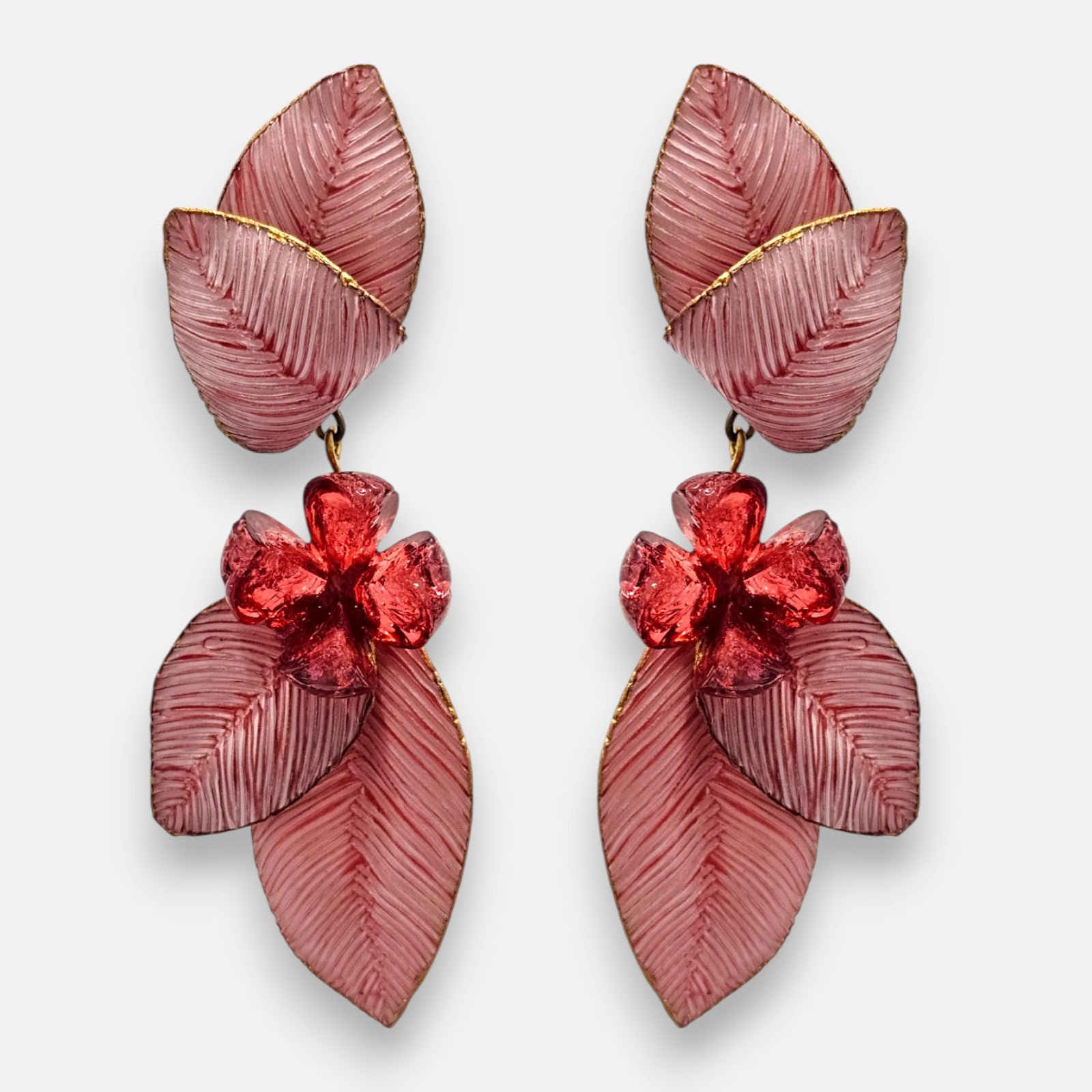par de pendientes largos de clip de Ciléa Paris sobre fondo claro, detallando su estructura de hojas estriadas rosa nácar con bordes dorados y una flor central color rojo rubí.