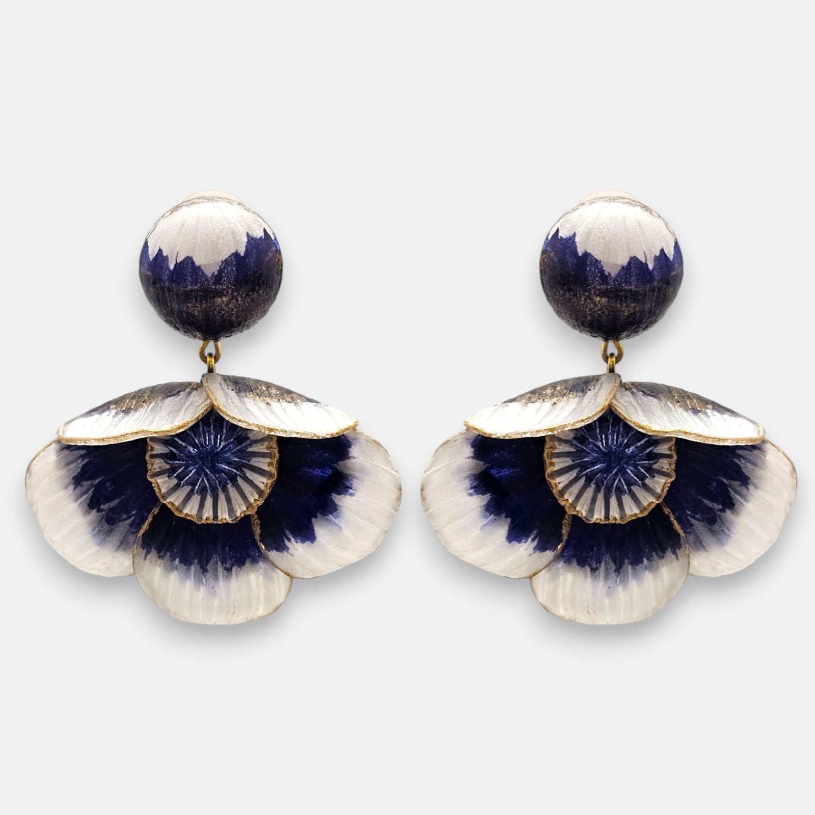 par de pendientes de presión con forma de flor de Ciléa Paris, detallando su botón superior redondo y sus pétalos degradados en blanco y azul cobalto con bordes dorados.