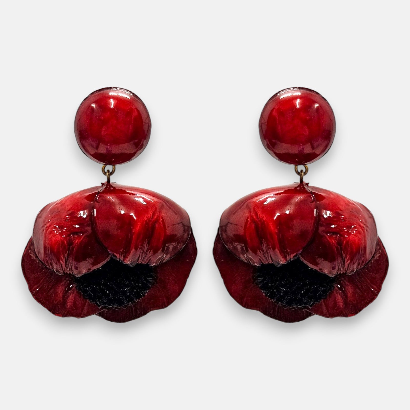 par de pendientes con forma de flor de amapola de Ciléa Paris sobre fondo claro, detallando su botón superior redondo y sus pétalos volumétricos en rojo carmín con centro negro.