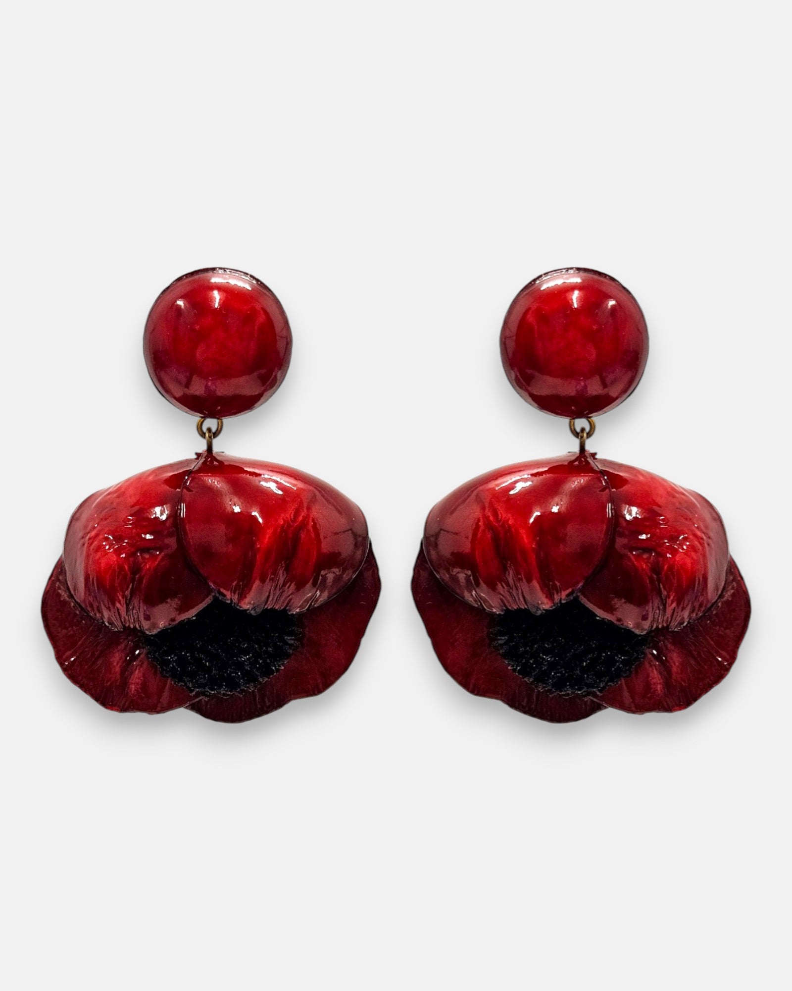 par de pendientes con forma de flor de amapola de Ciléa Paris sobre fondo claro, detallando su botón superior redondo y sus pétalos volumétricos en rojo carmín con centro negro.