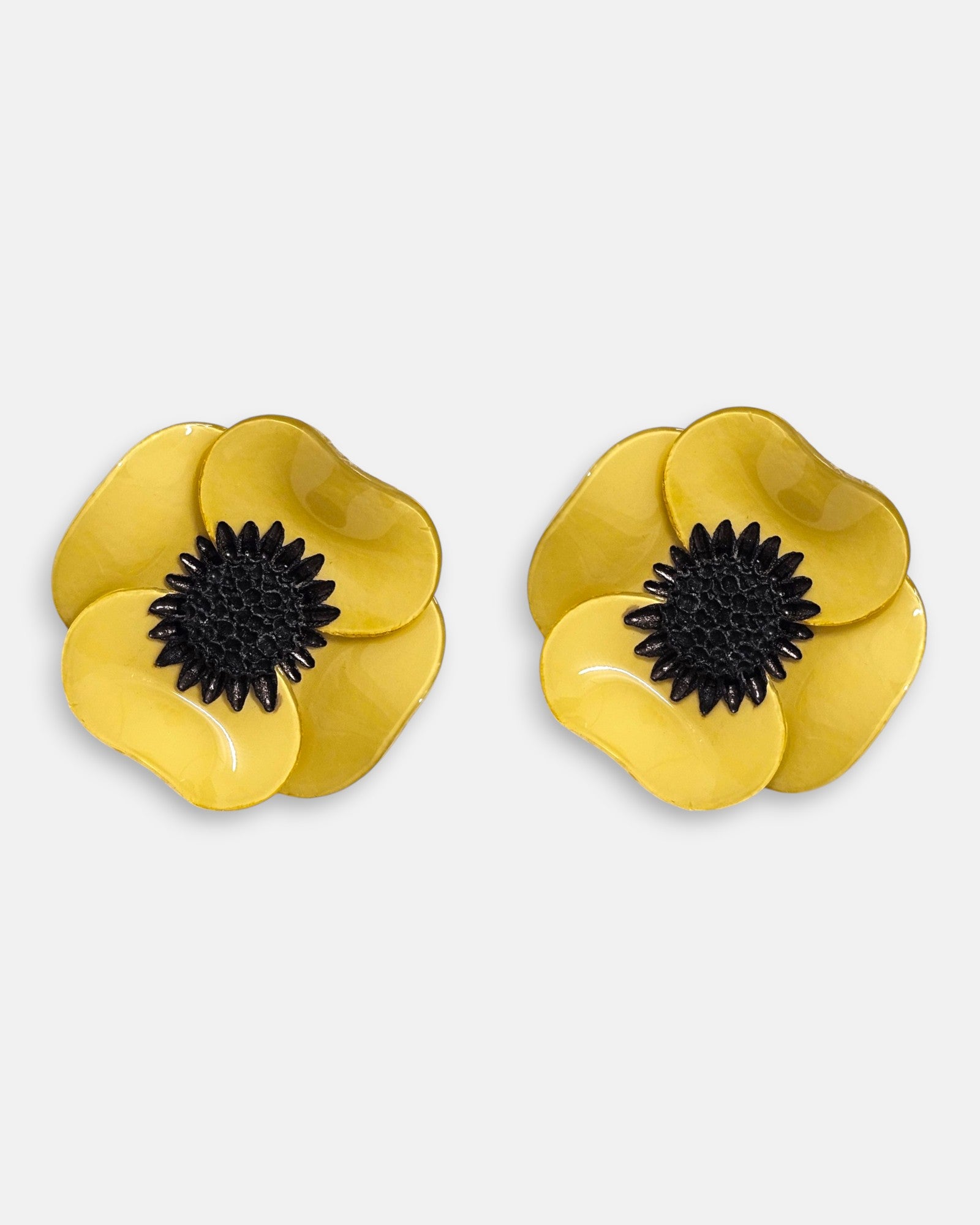par de pendientes de botón con forma de flor de amapola de Ciléa Paris sobre fondo claro, detallando sus pétalos volumétricos en amarillo mostaza brillante con un gran centro negro.