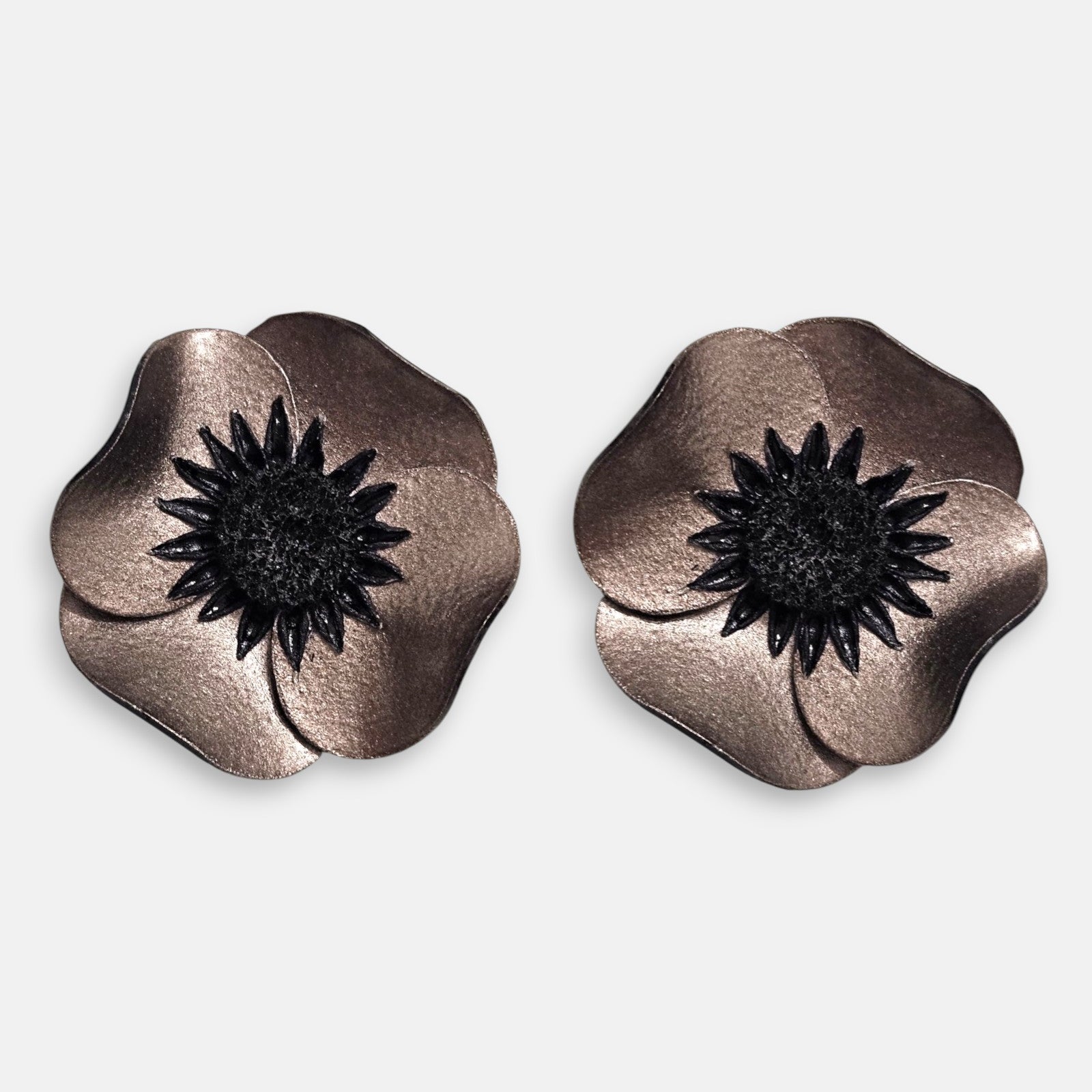 par de pendientes de clip con forma de flor de amapola de Ciléa Paris, detallando sus pétalos de resina metalizada en tono bronce y su gran centro negro estrellado.