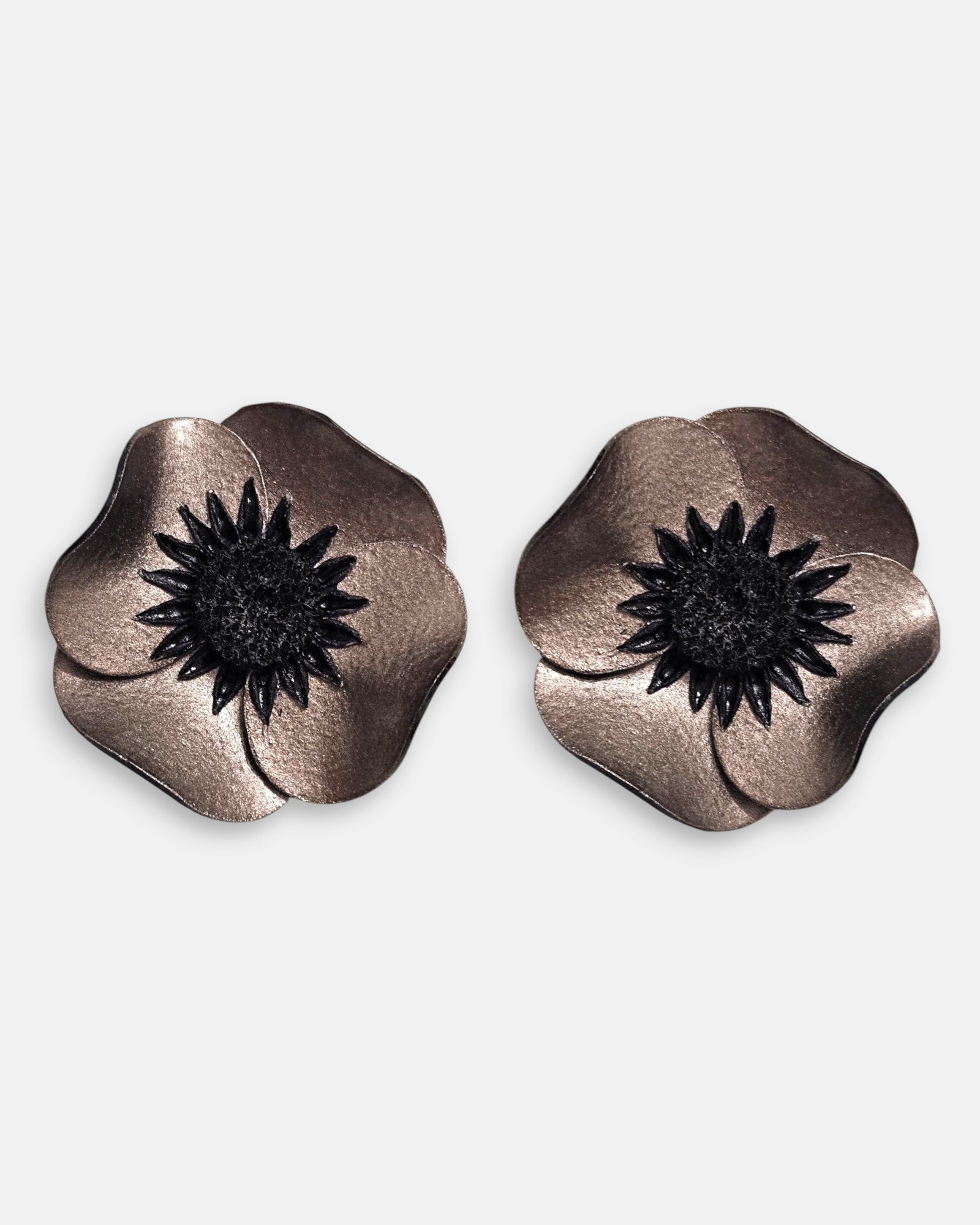 par de pendientes de clip con forma de flor de amapola de Ciléa Paris, detallando sus pétalos de resina metalizada en tono bronce y su gran centro negro estrellado.