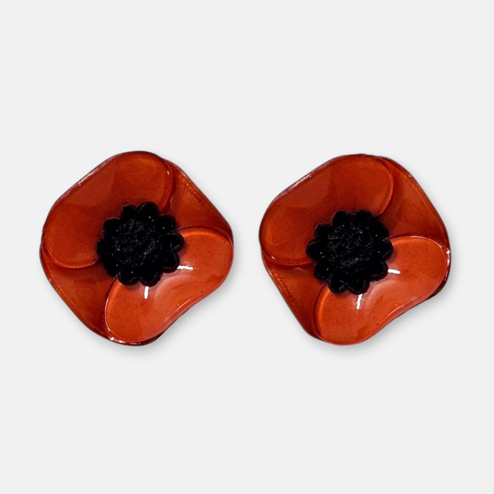 par de pendientes pequeños de presión con forma de flor de amapola de Ciléa Paris, detallando sus pétalos de resina esmaltada en tono rojo pasión brillante y su centro negro estrellado.